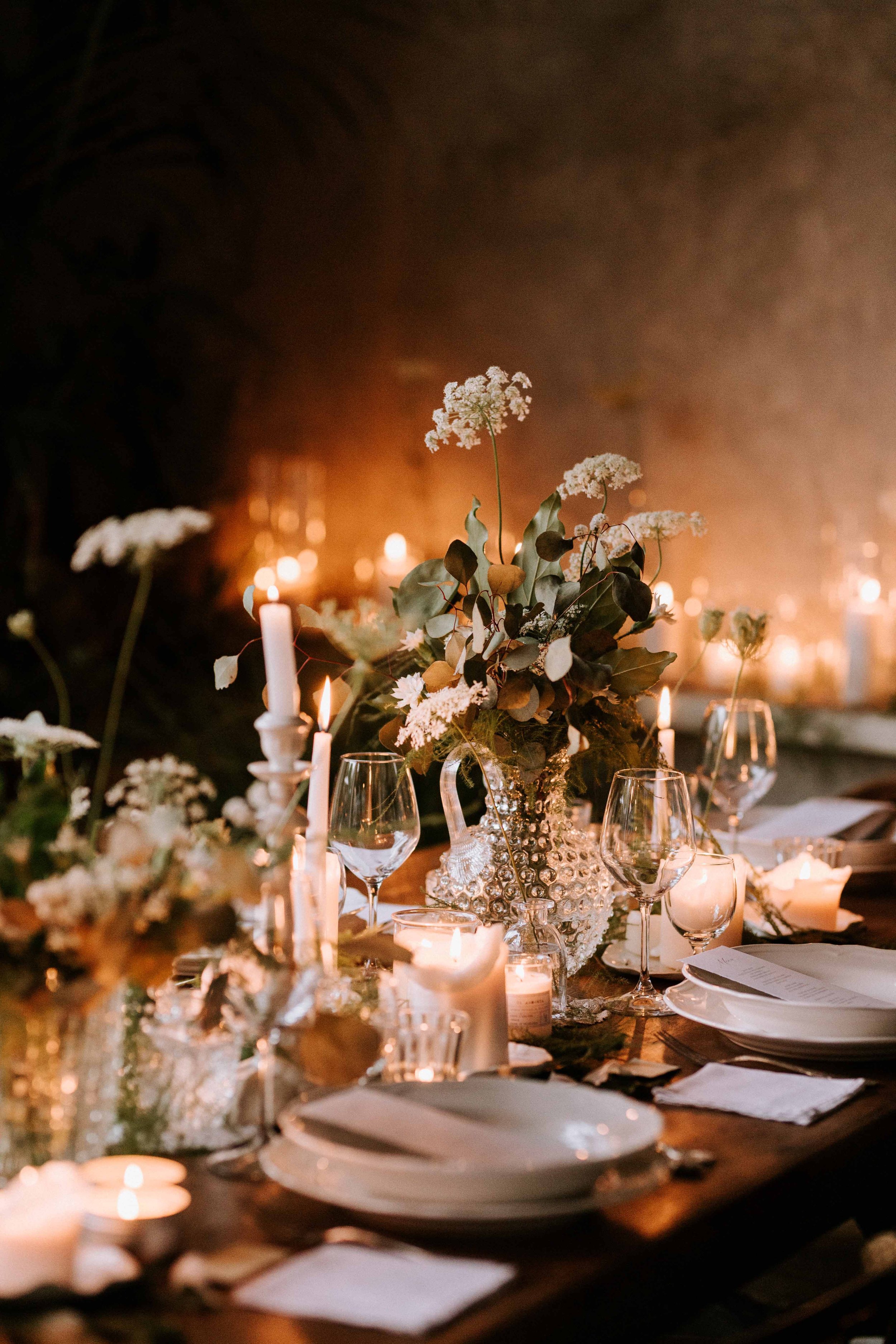 A beautifully decorated table with white flowers, candles, and glassware in a warm, dimly lit setting.