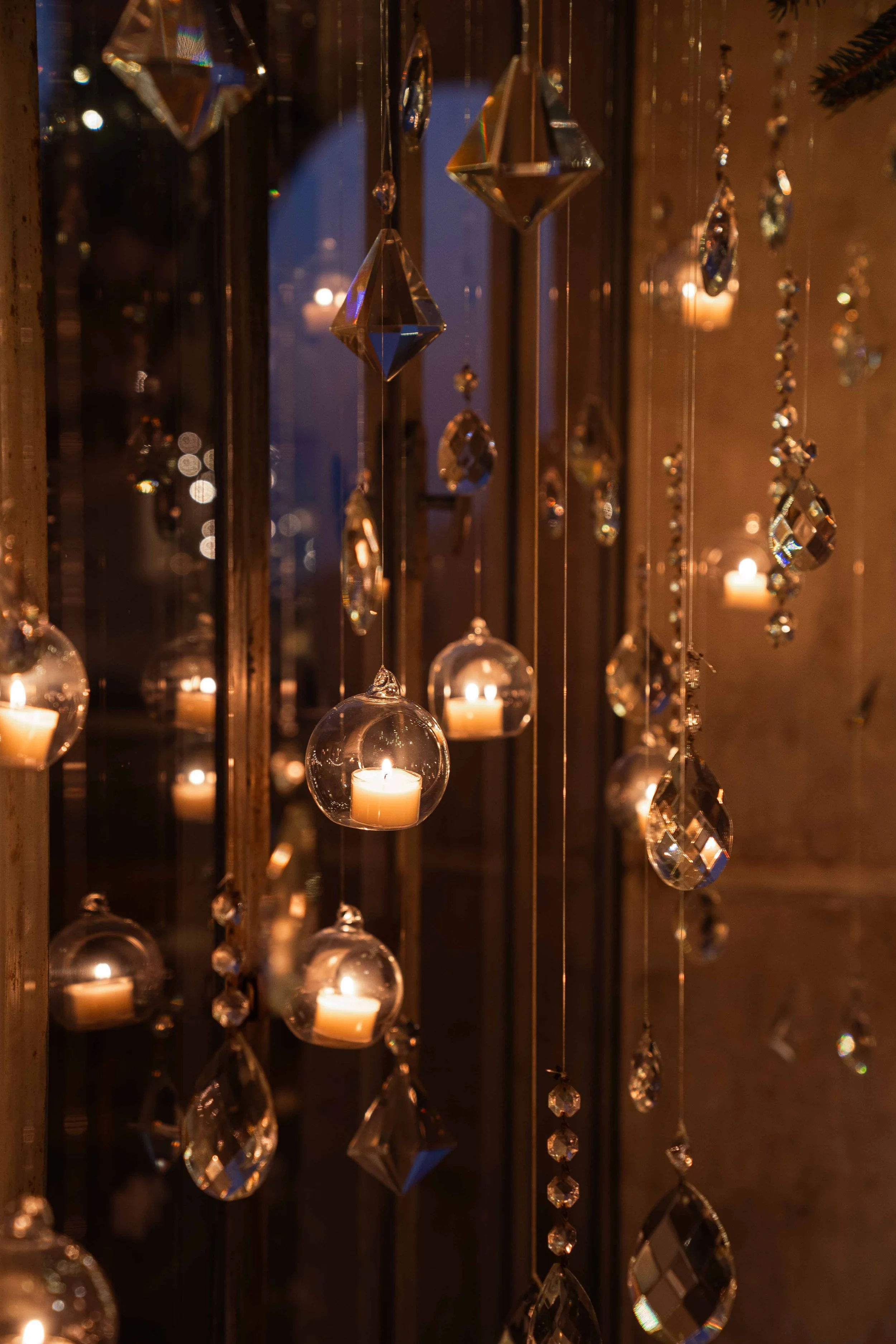 Hanging crystal and glass ornaments with small candles inside glass globes, dimly lit.