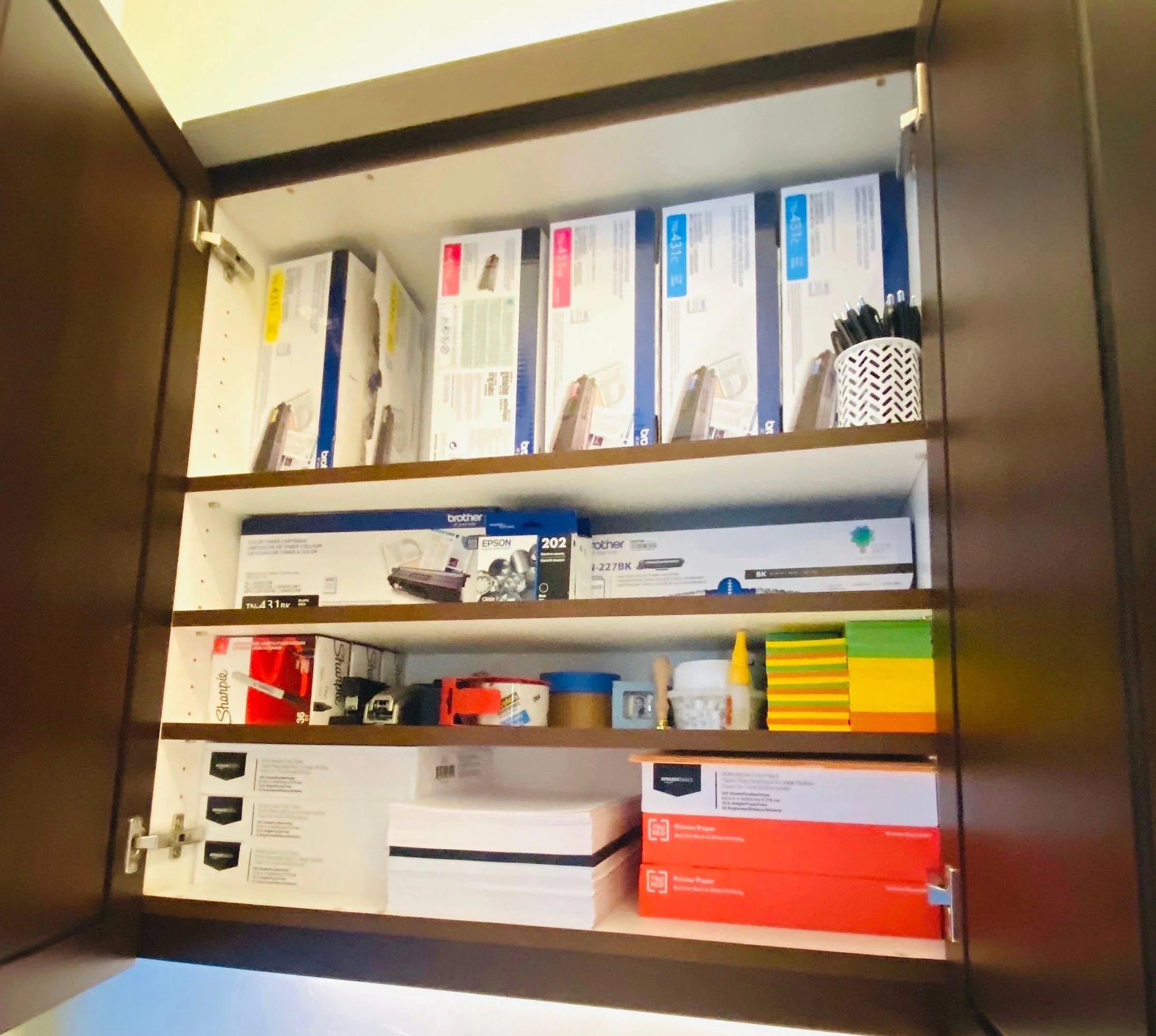 Sorted office cabinet organization featuring designated zones for sticky notes, printer ink, paper packs, and tape supplies in Park City, Utah.