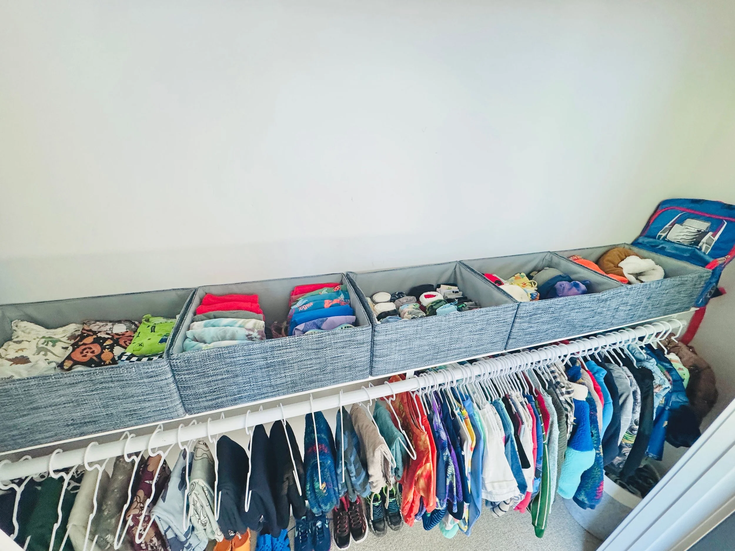 Organized boys' bedroom closet featuring a neat overview of custom hung clothing and color-coded storage bins for folded items in Park City, Utah.
