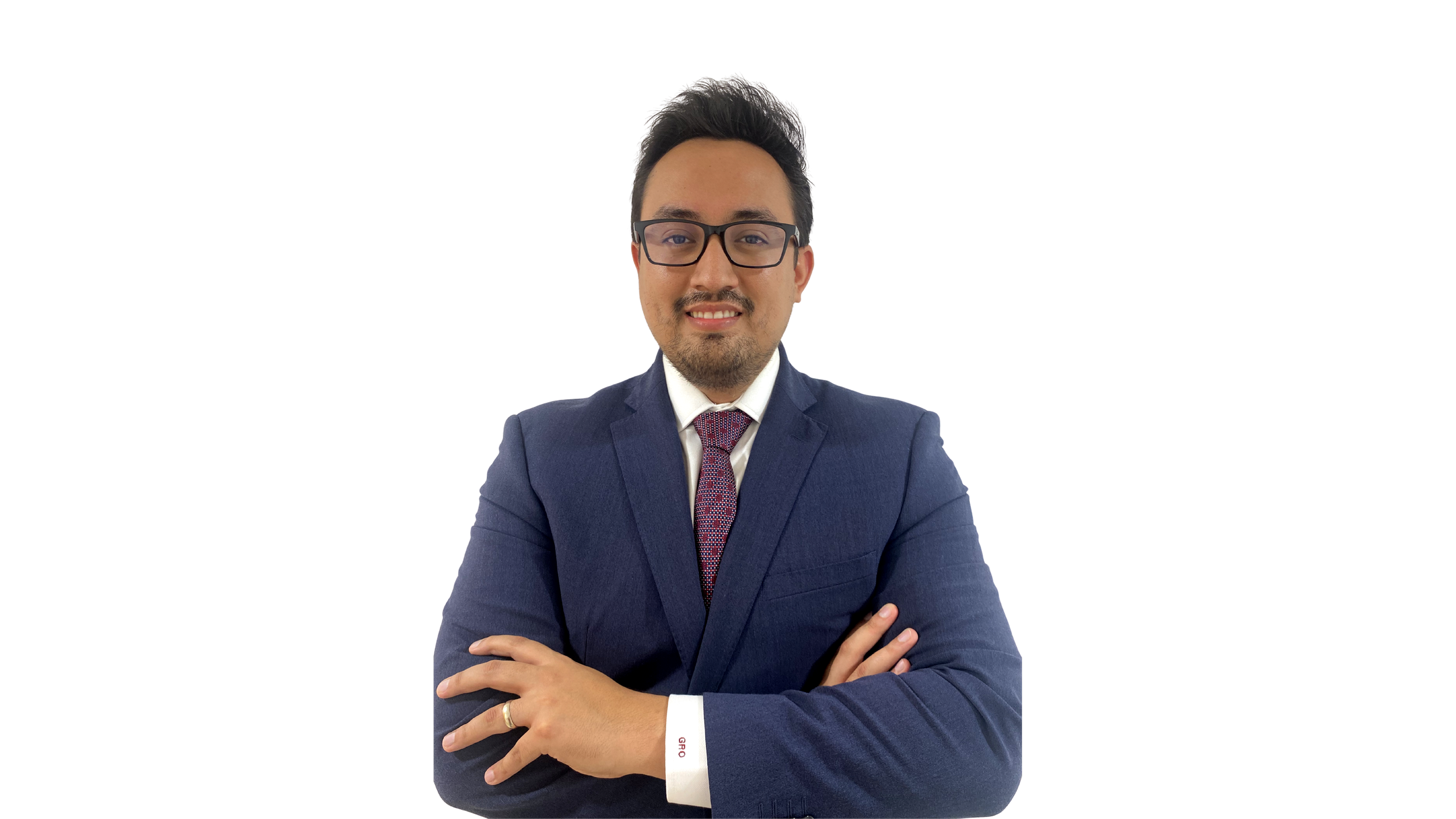 Hombre con gafas, traje azul, camisa blanca y corbata, sonriendo con brazos cruzados, fondo negro.