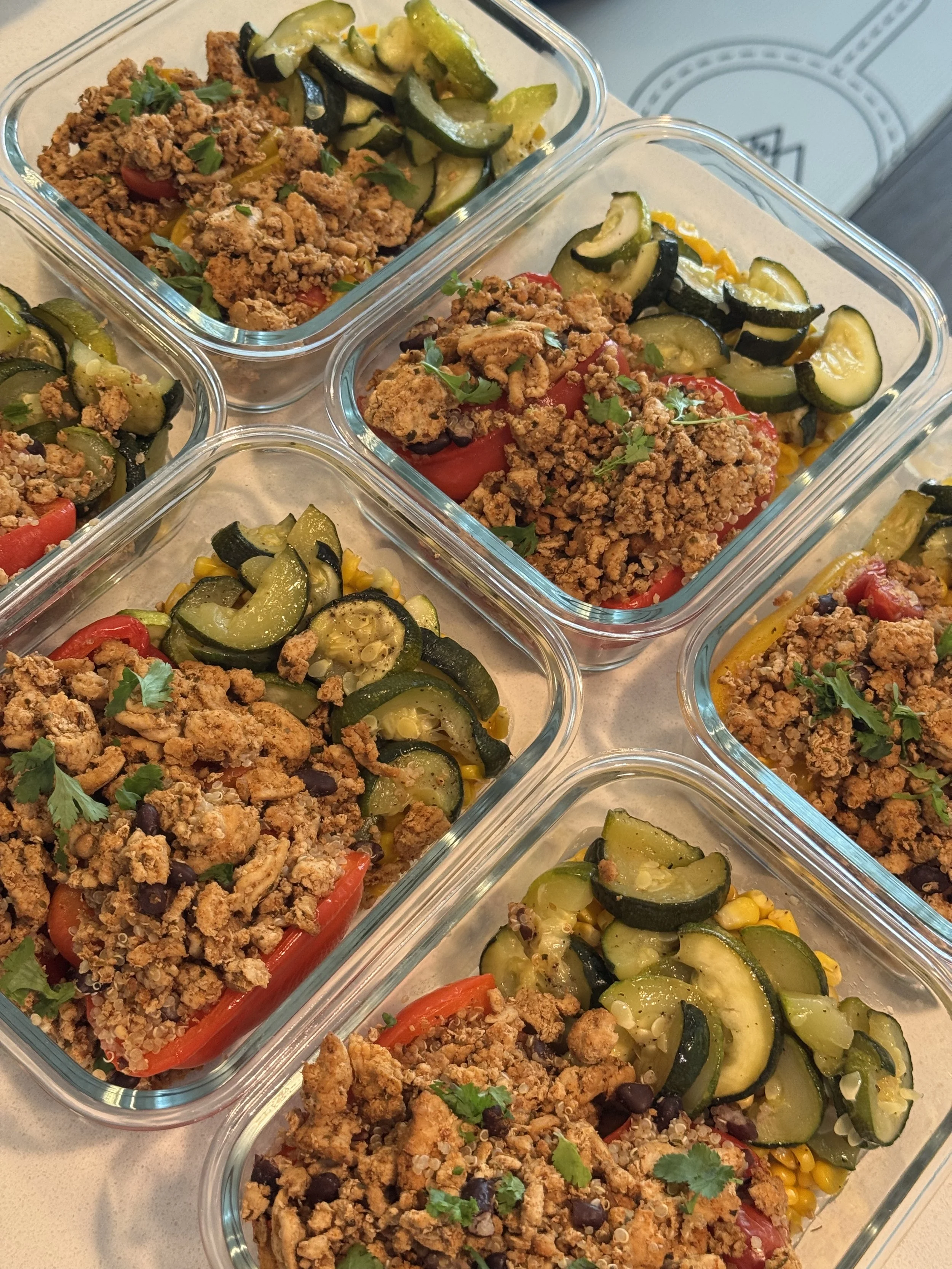 Several glass containers filled with baked dishes. Each contains a mixture of cooked vegetables including zucchini, yellow squash, corn, and red bell peppers, topped with seasoned ground meat or crumbled topping, garnished with fresh cilantro or parsley.