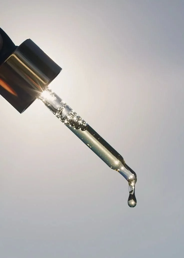 Sérum ou huile dans une pipette, avec des gouttelettes brillant sous une lumière forte.