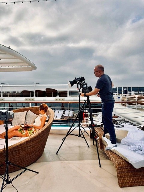 Photographer filming a woman on a balcony of a cruise ship during the daytime, with cloudy skies overhead.