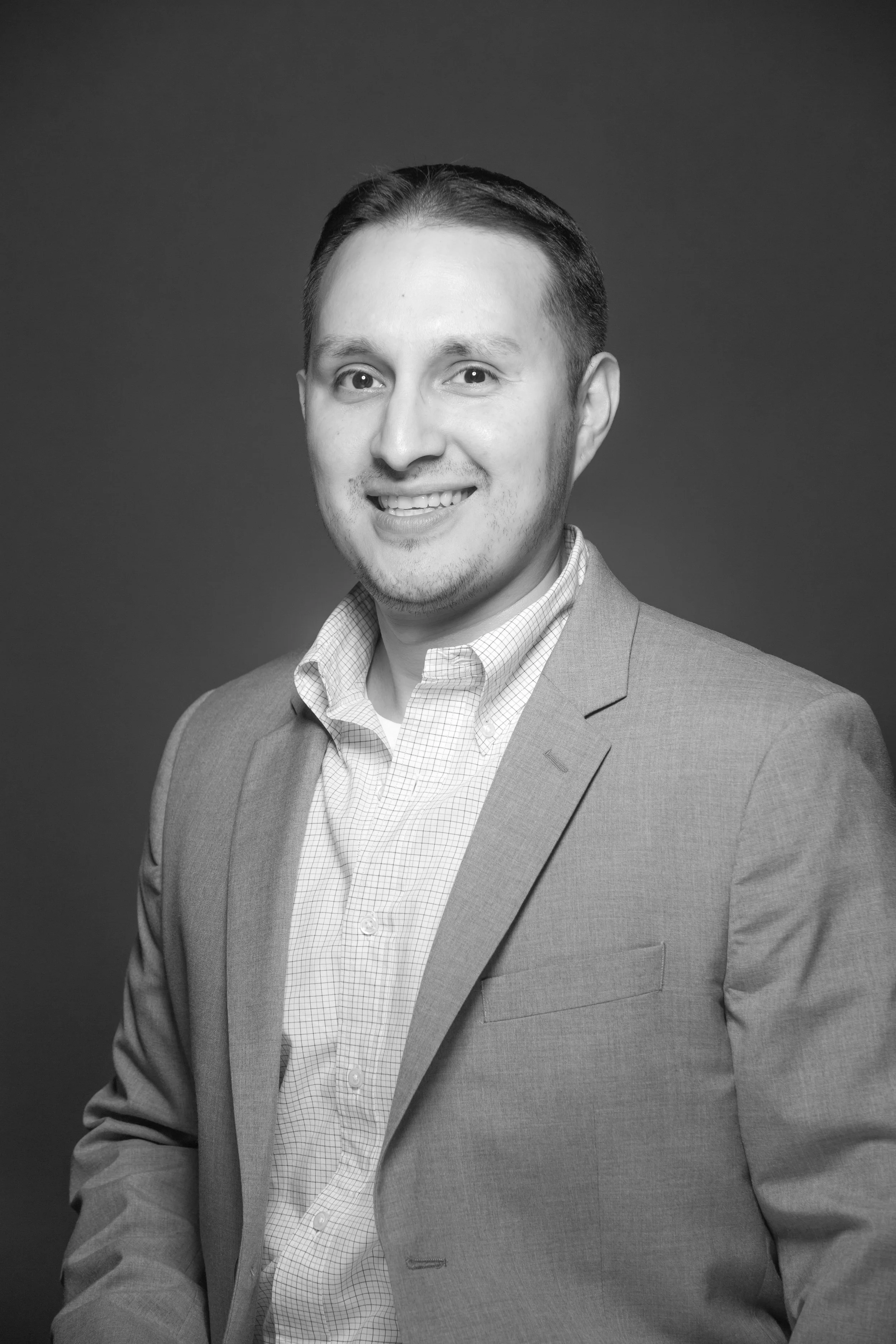 Black and white portrait of a smiling man wearing a suit jacket and collared shirt, looking at the camera against a plain background.