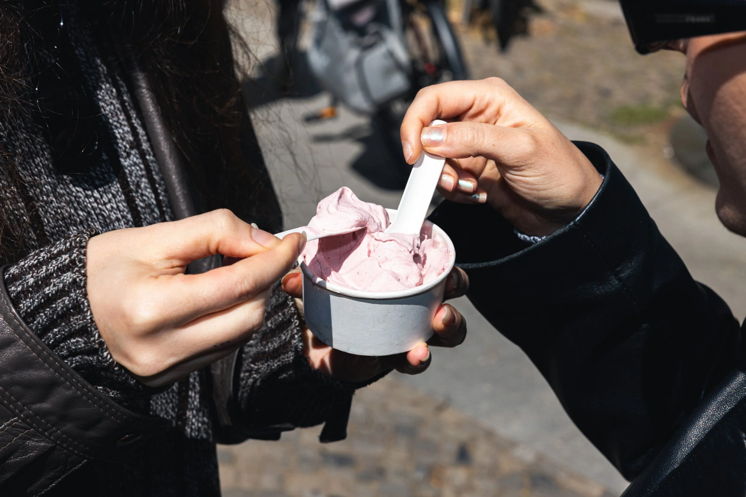 Two people sharing a cup of pink ice cream outdoors on a sunny day.