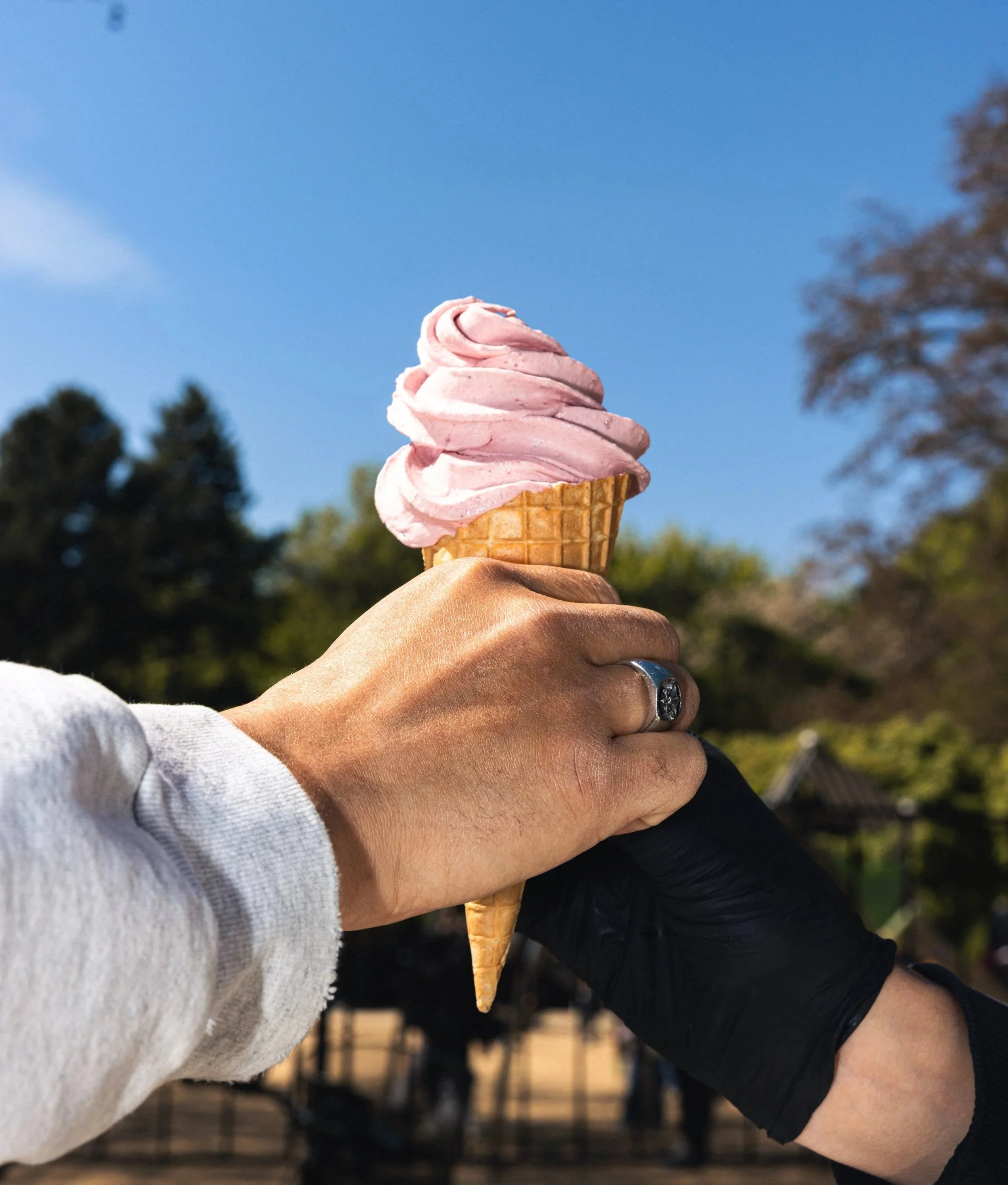A person holding an ice cream cone with pink soft serve ice cream outdoors on a sunny day.