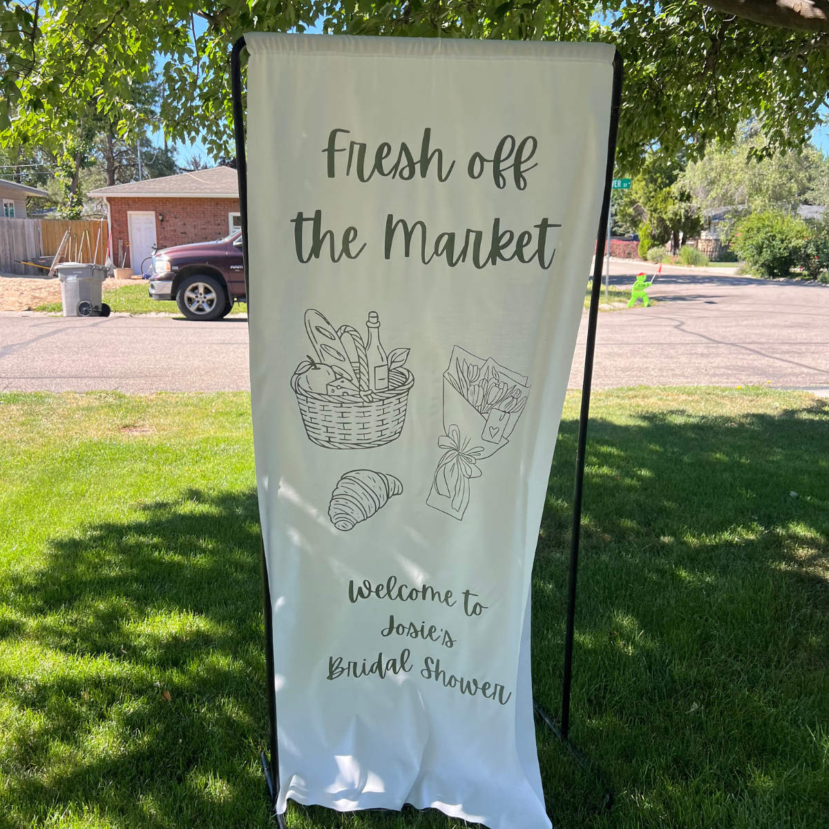 Outdoor bridal shower sign with illustrations of a picnic basket, croissant, and flowers, welcoming guests to Josie's bridal shower.
