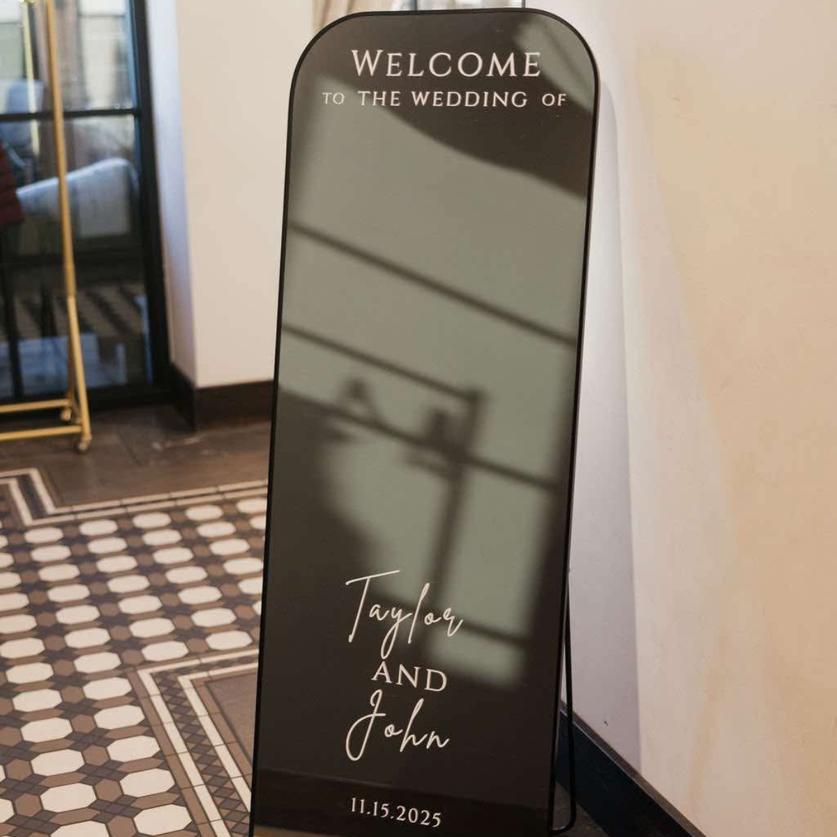 A vertical wedding sign with a reflective surface, welcoming guests to the wedding of Taylor and John on November 15, 2025.