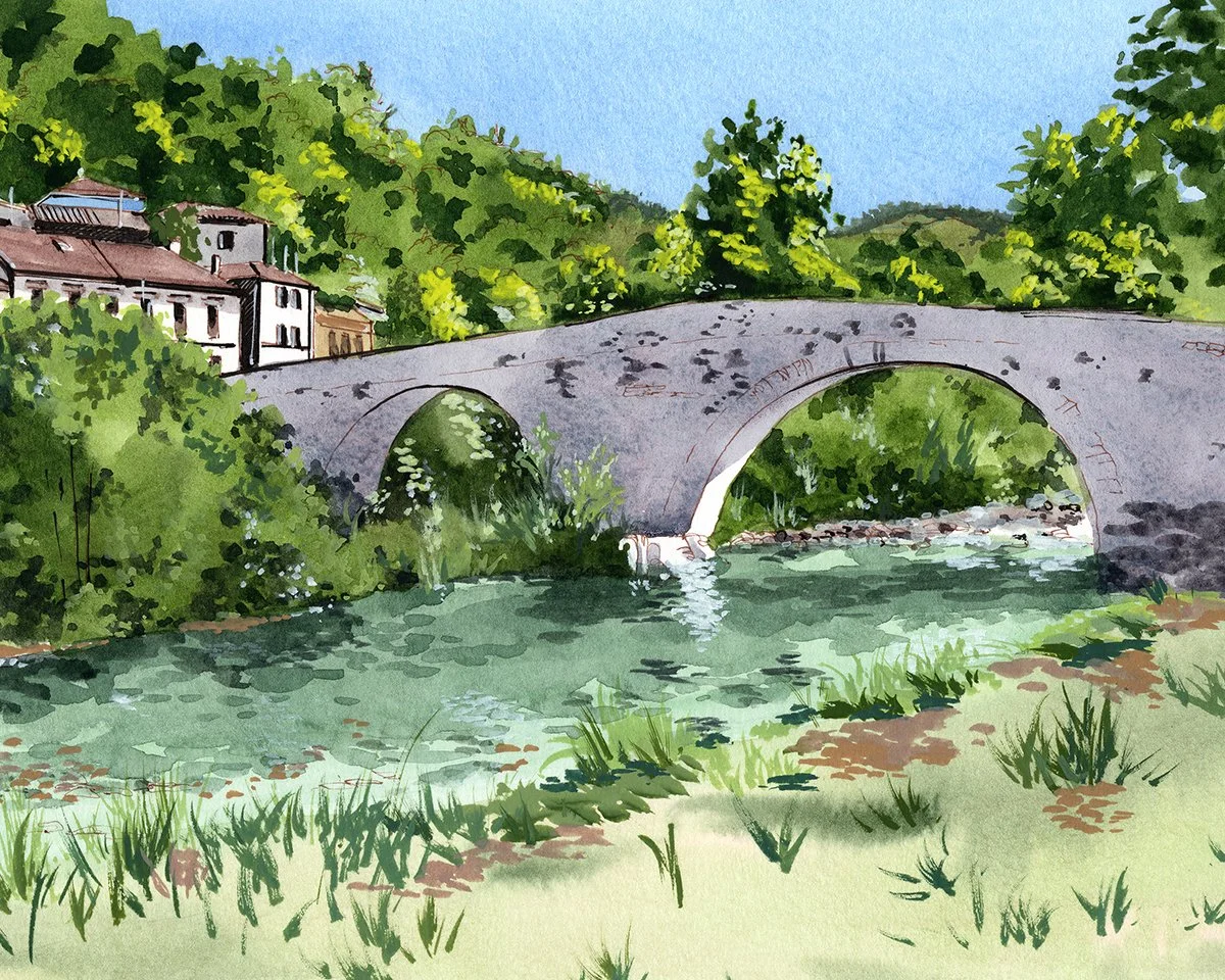 Puente de piedra sobre un río, rodeado de vegetación y árboles verdes, con colinas y casas en el fondo bajo un cielo azul.