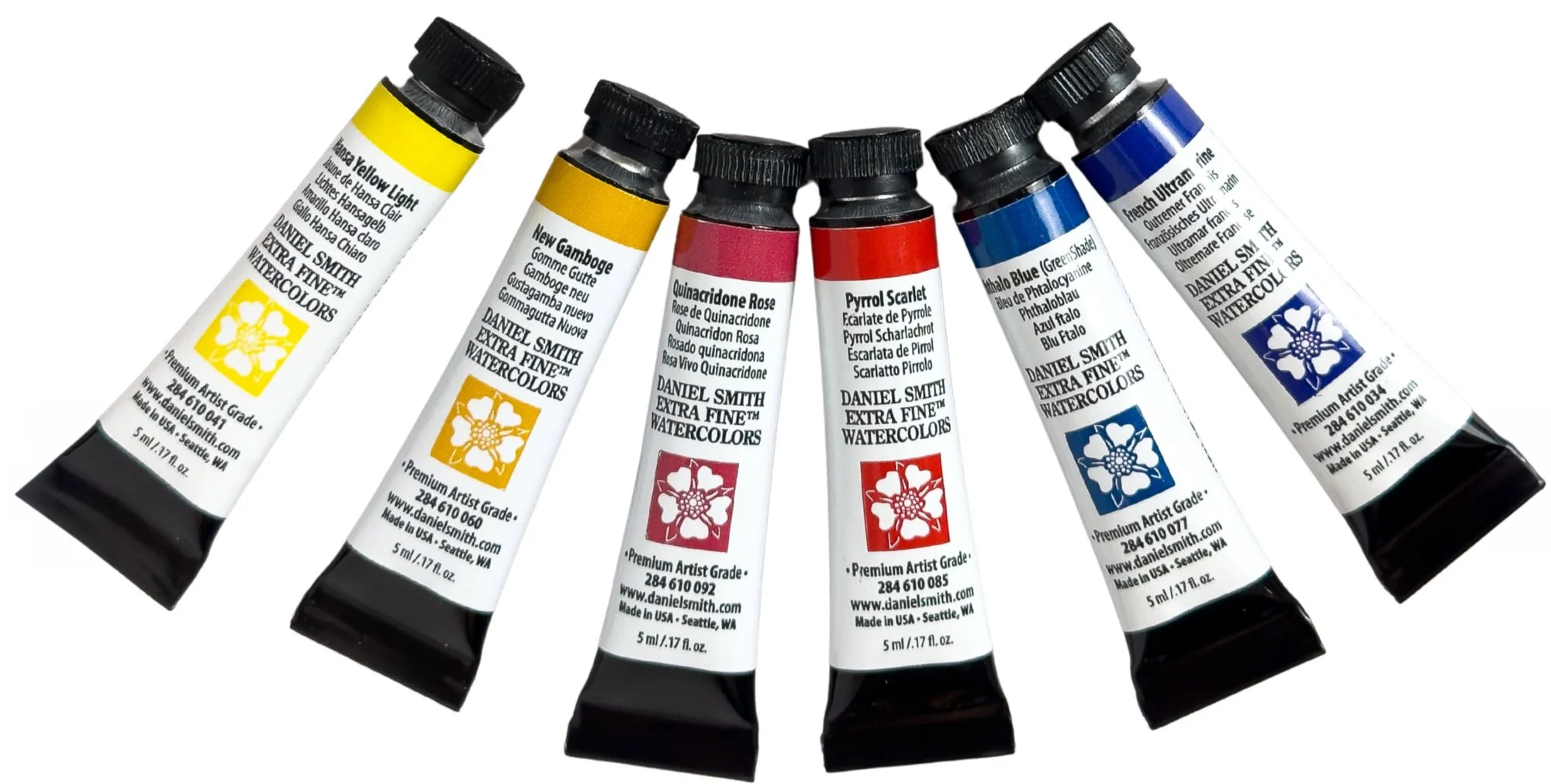 Tubos de acuarelas de diferentes colores, incluyendo amarillo, ocre, rosa, rojo, azul y gris, con etiquetas que indican los nombres y detalles del producto.