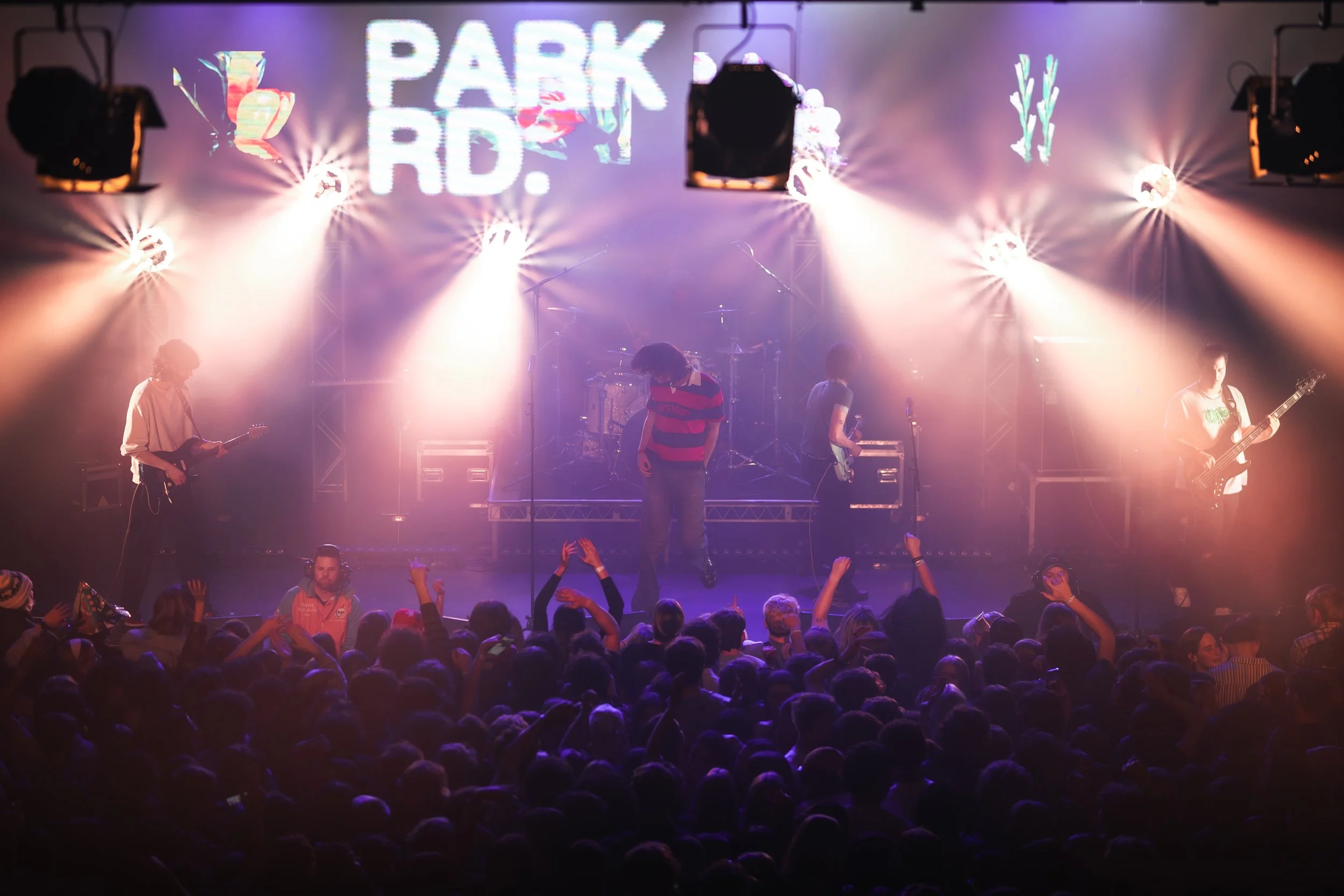 A live concert with a band performing on stage, illuminated by colorful lights and surrounded by an audience.