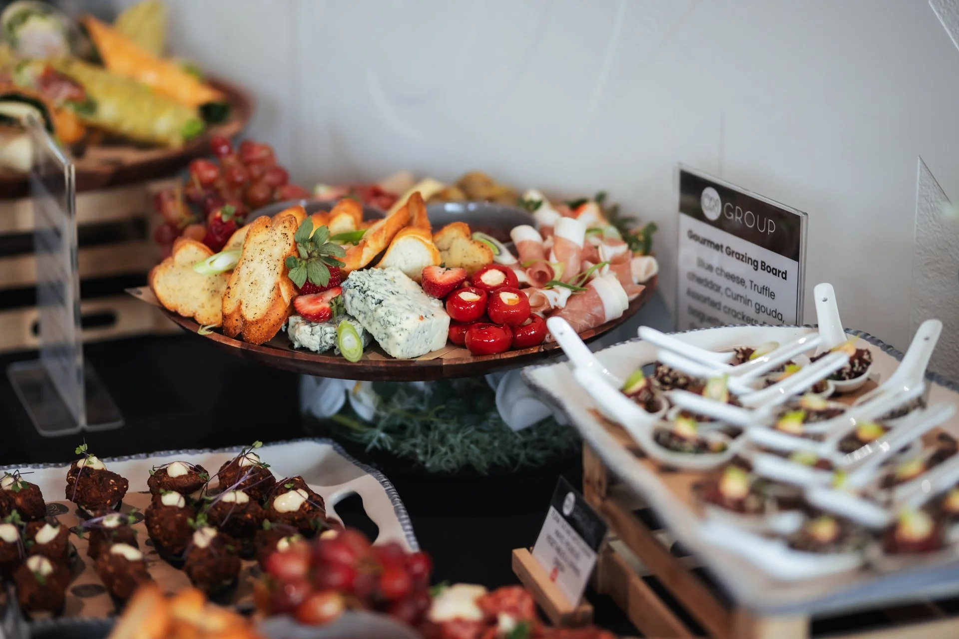 Gourmet grazing board with cheeses, crackers, strawberries, and garnishes on a table, with smaller dishes of appetisers nearby, showcasing Haere-roa's catering