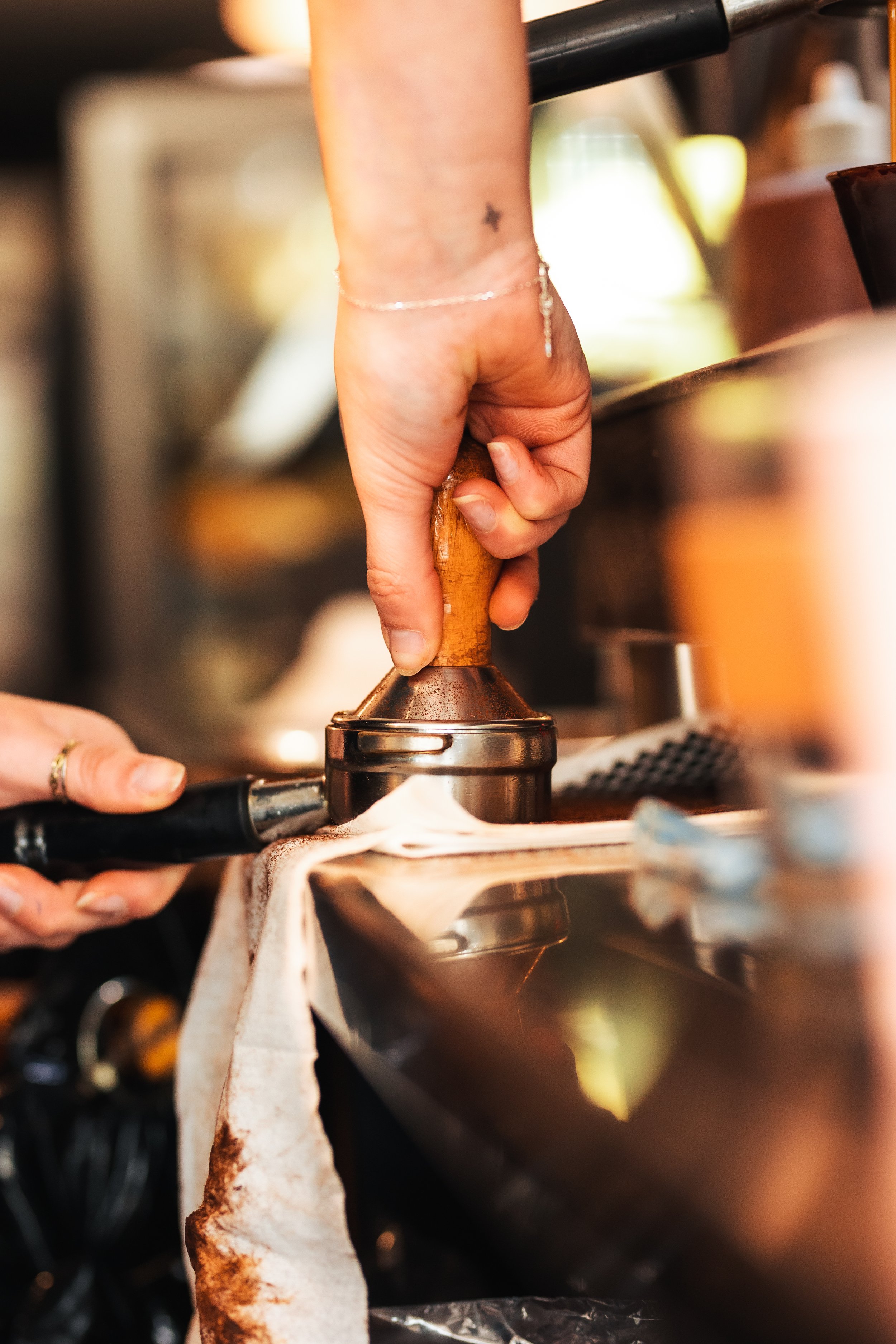 Close-up of a person's hand pressing down on a black handle with a wooden top, on a stovetop with a cloth hanging from the side.
