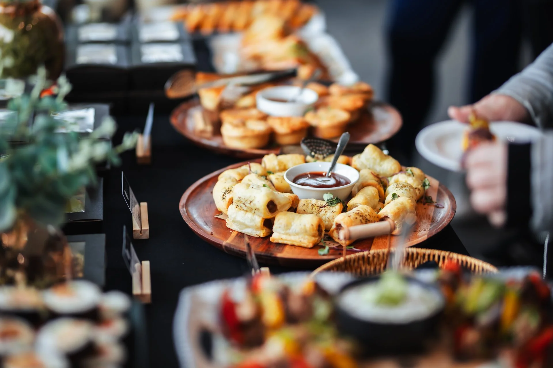 A buffet table with different kinds of appetizers, including stuffed rolls with sauce, served on wooden and ceramic plates.