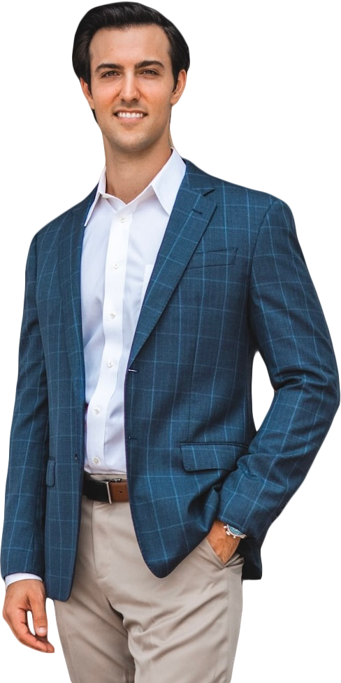 Garret Greco stands in front of a black door, wearing a blue checkered blazer, white dress shirt, and beige pants, smiling at the camera.
