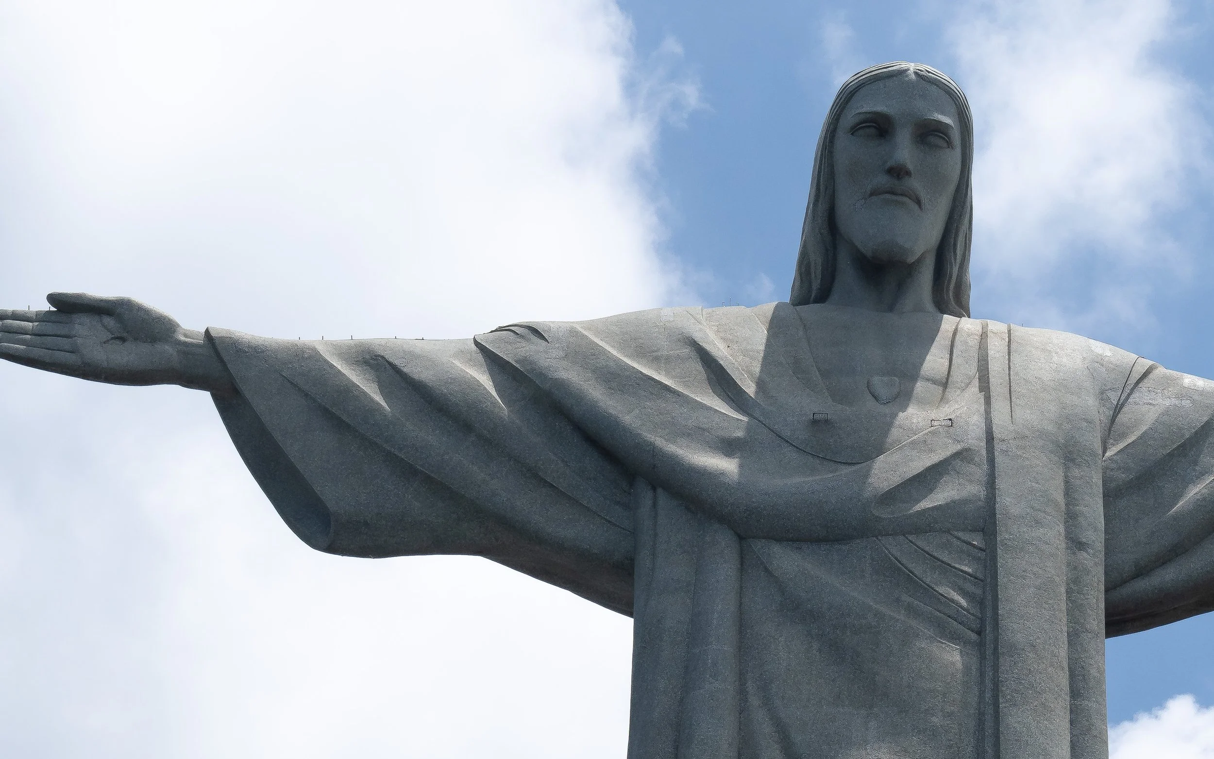 Close-up of the Christ the Redeemer statue in Rio de Janeiro, Brazil, with outstretched arms against a partly cloudy sky.