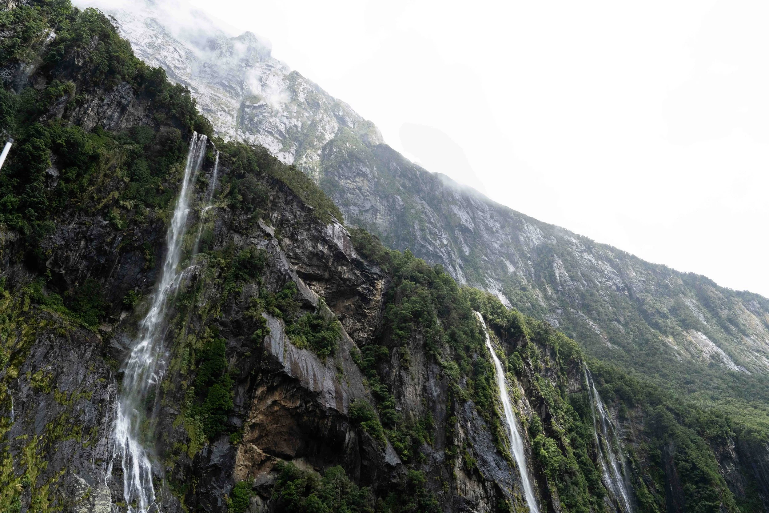 A mountain with multiple waterfalls cascading down its rocky, green slopes, with mist and clouds around the peaks.