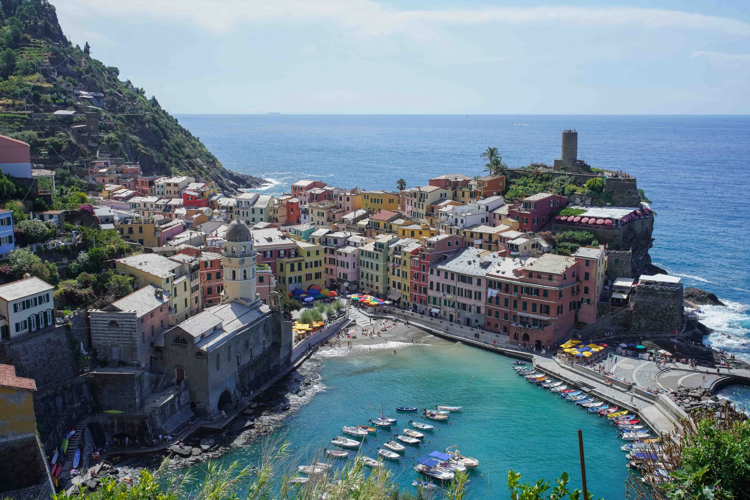 Vernazza, Cinque Terre, Italy, a colorful Italian coastal city, a small harbor with boats, and a castle on a rocky outcrop overlooking the ocean.