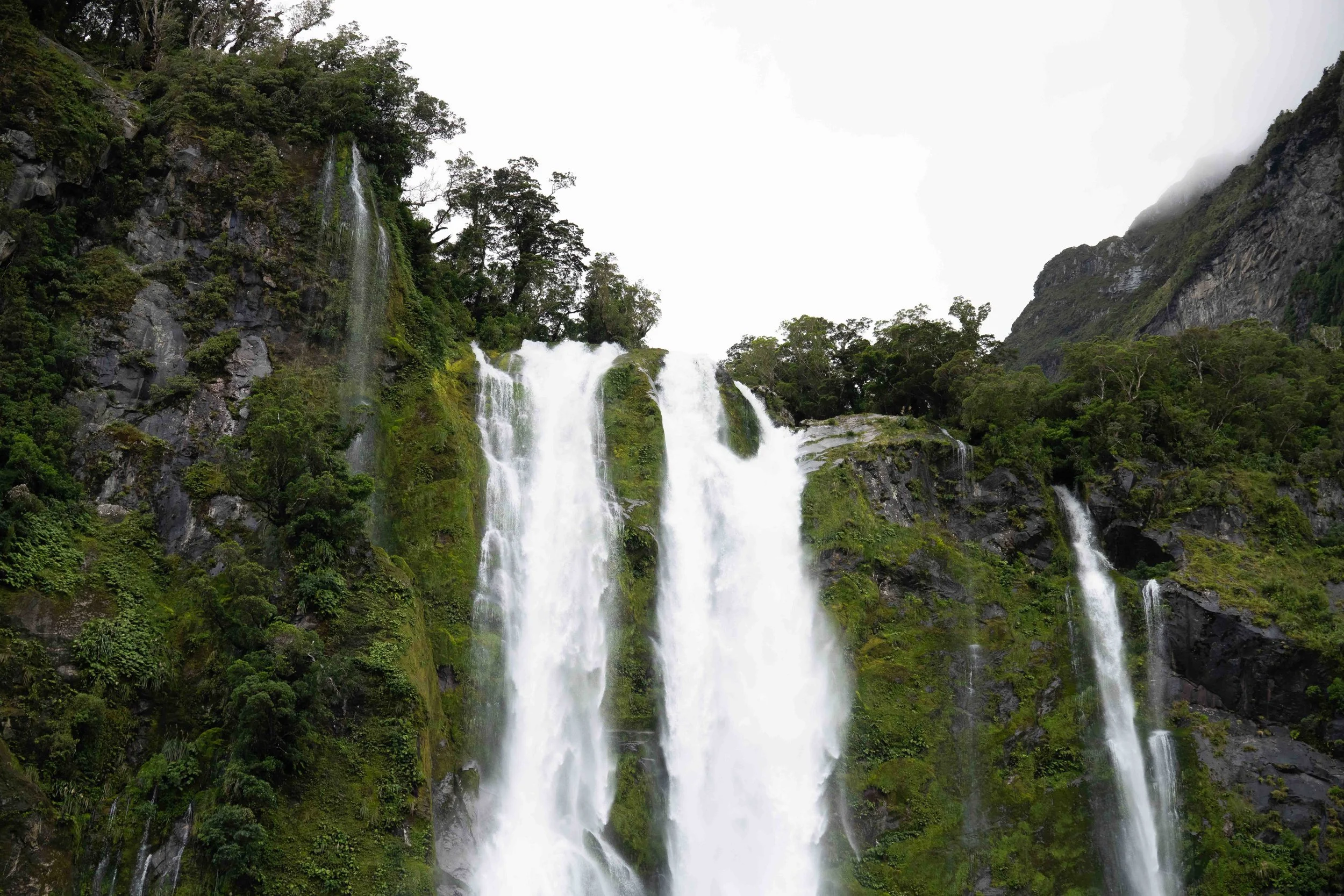 A waterfall cascading down a lush green mountainside surrounded by dense jungle and trees.