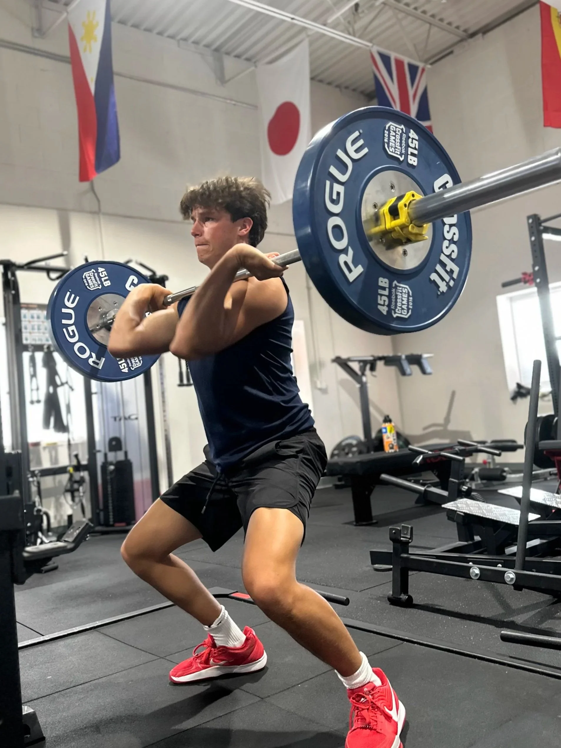 A man in athletic clothing lifting a barbell with weights in a gym.