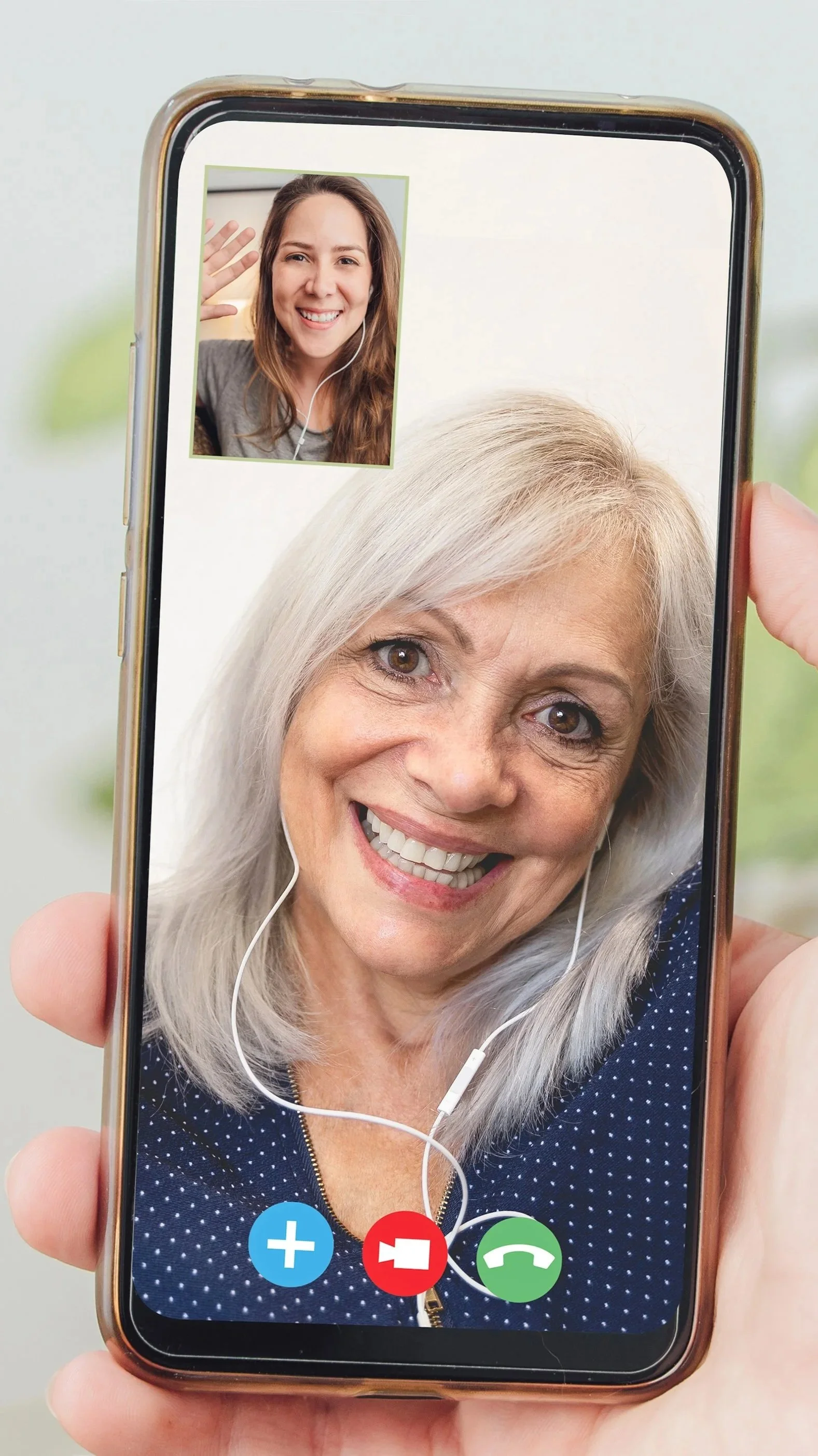 Close-up of a smartphone screen displaying a video call with an older woman with gray hair smiling, and a smaller inset window showing a young woman with brown hair waving and smiling.