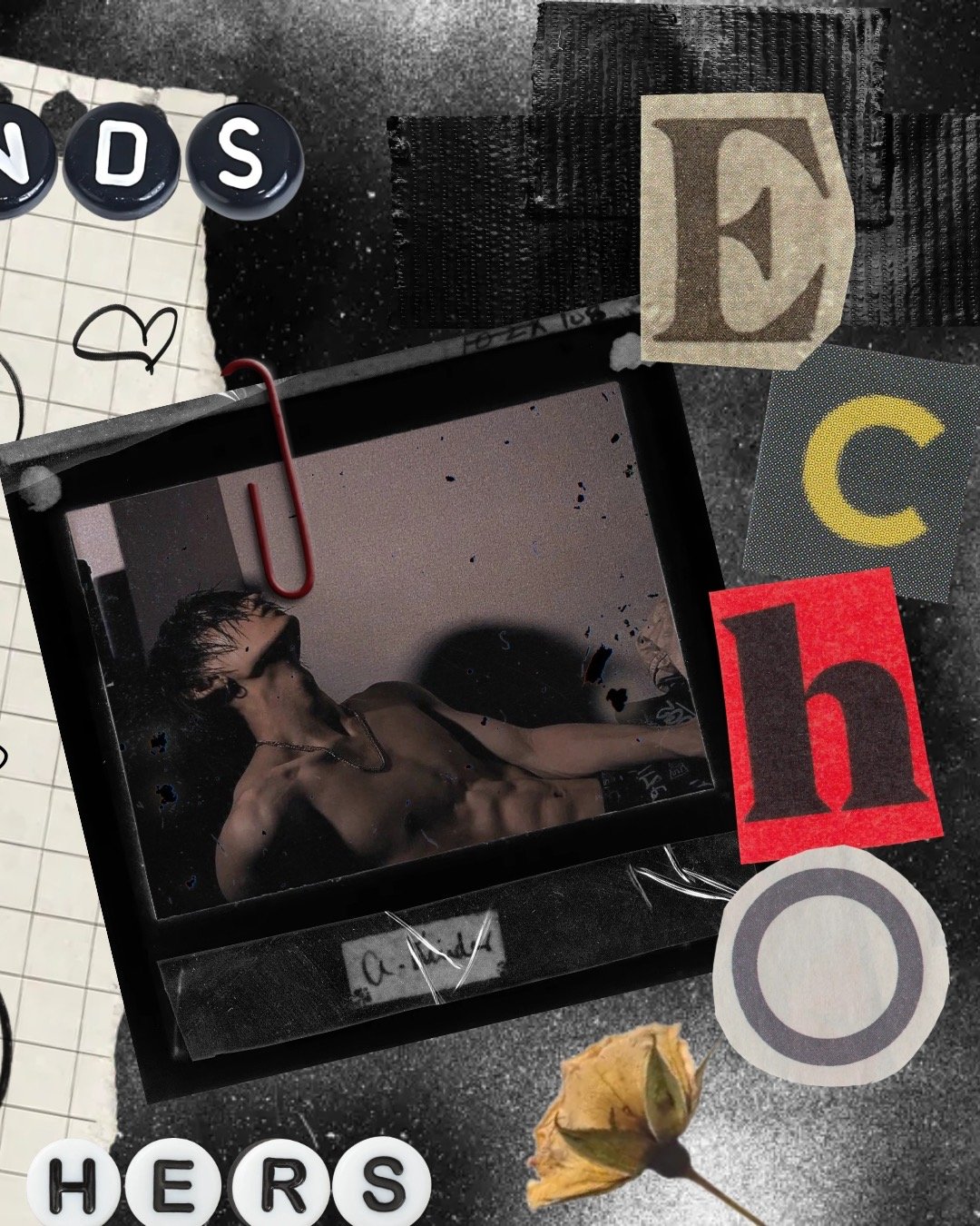 A Polaroid photo of a shirtless young man with glasses and earrings, surrounded by decorative letters, papers, and objects on a black surface.