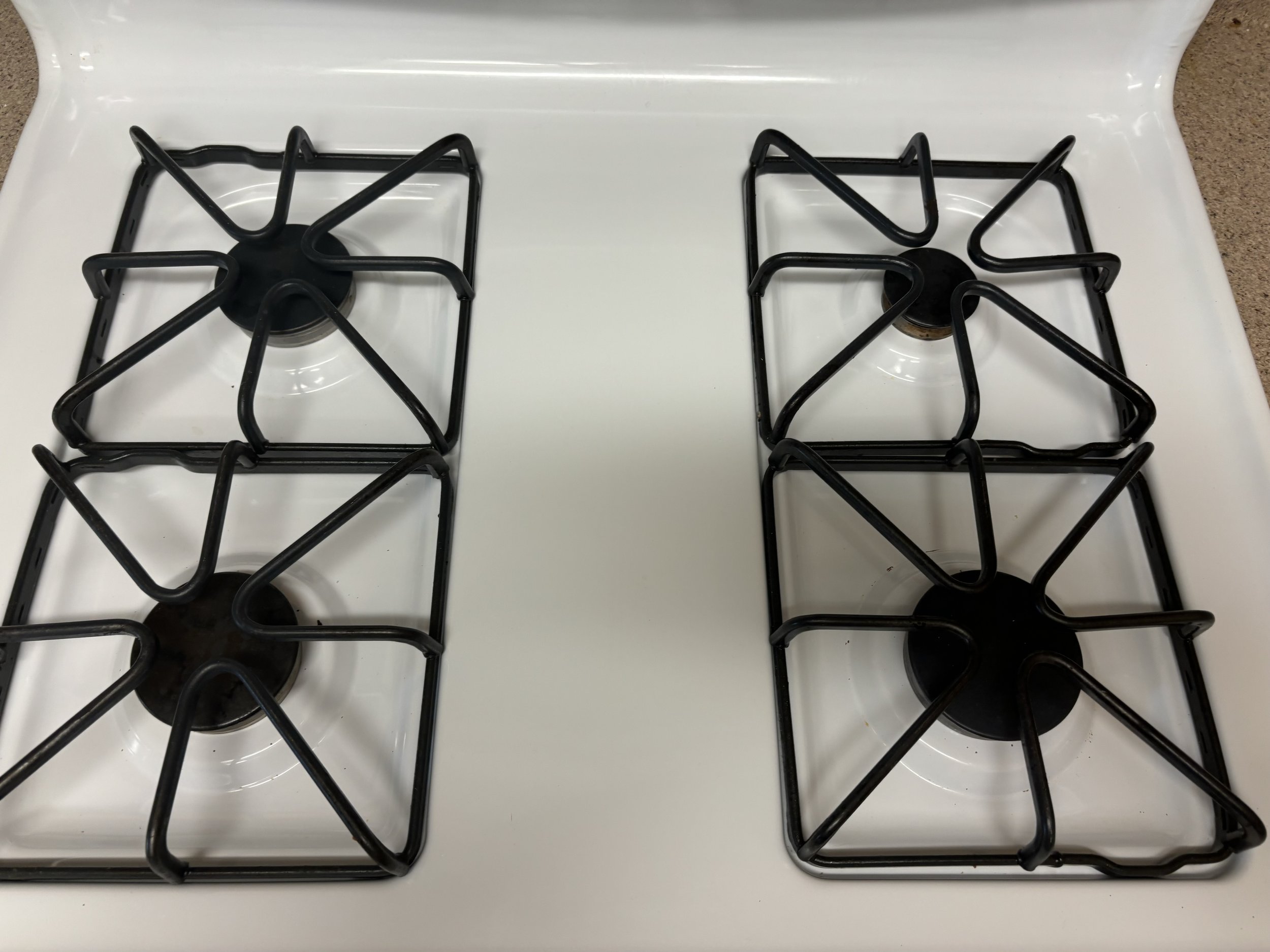 Two black gas stove burners on a white stovetop with one burner missing a grate.