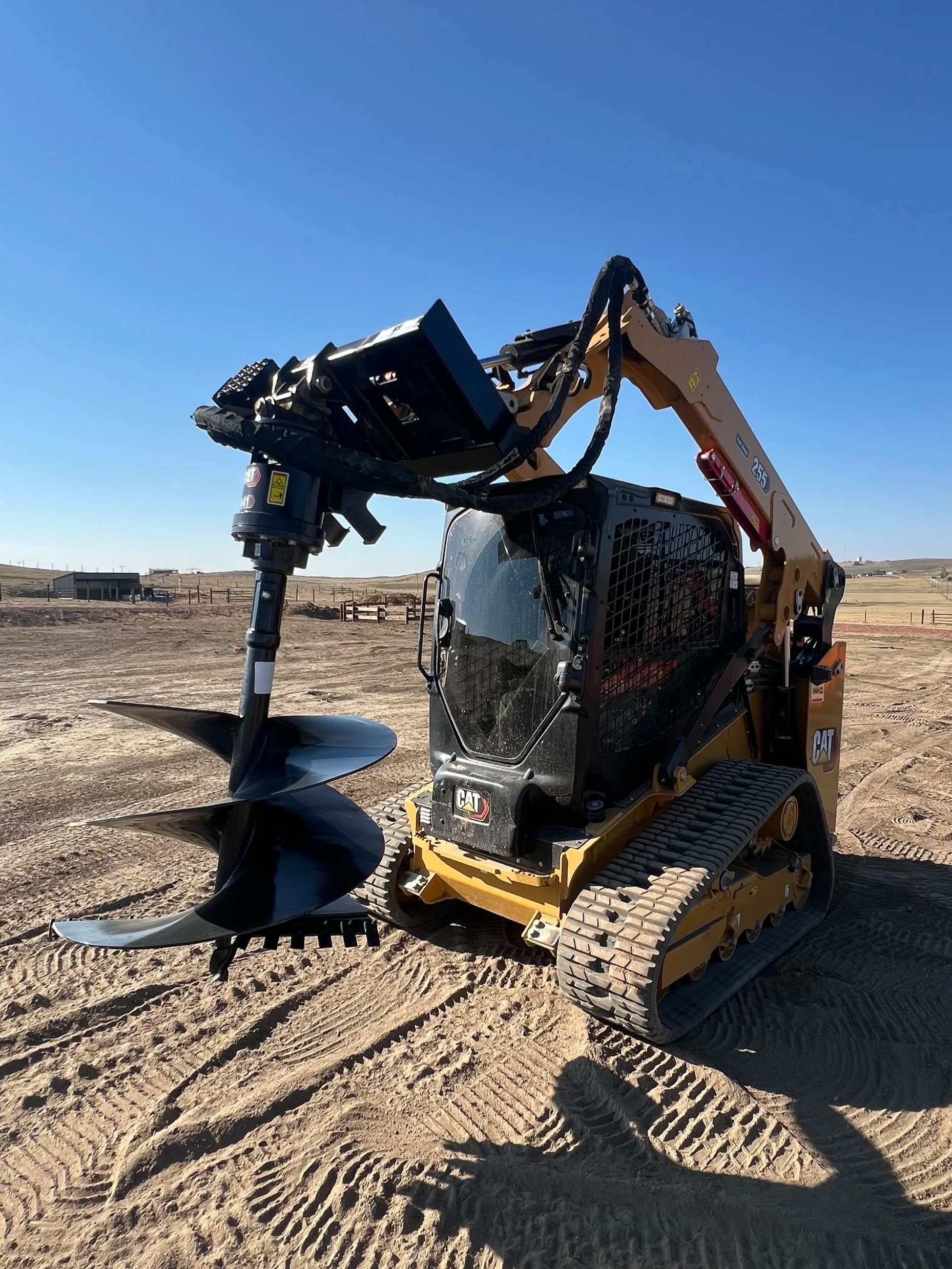 Close-up of a piece of construction equipment with black hydraulic hoses and a black control handle resting on a wooden pallet on dry, cracked ground.