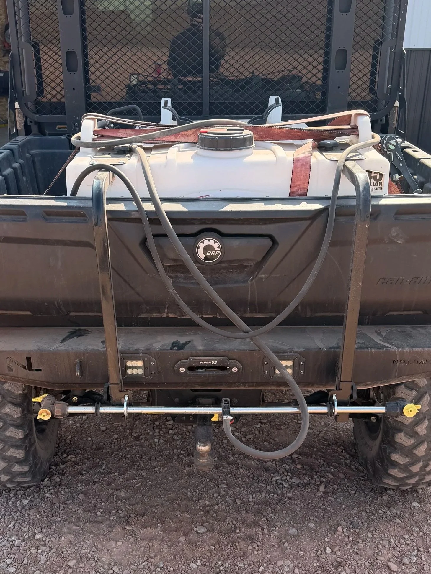Front view of an off-road utility vehicle with a water tank mounted in the bed, hoses, and equipment, on a gravel surface.