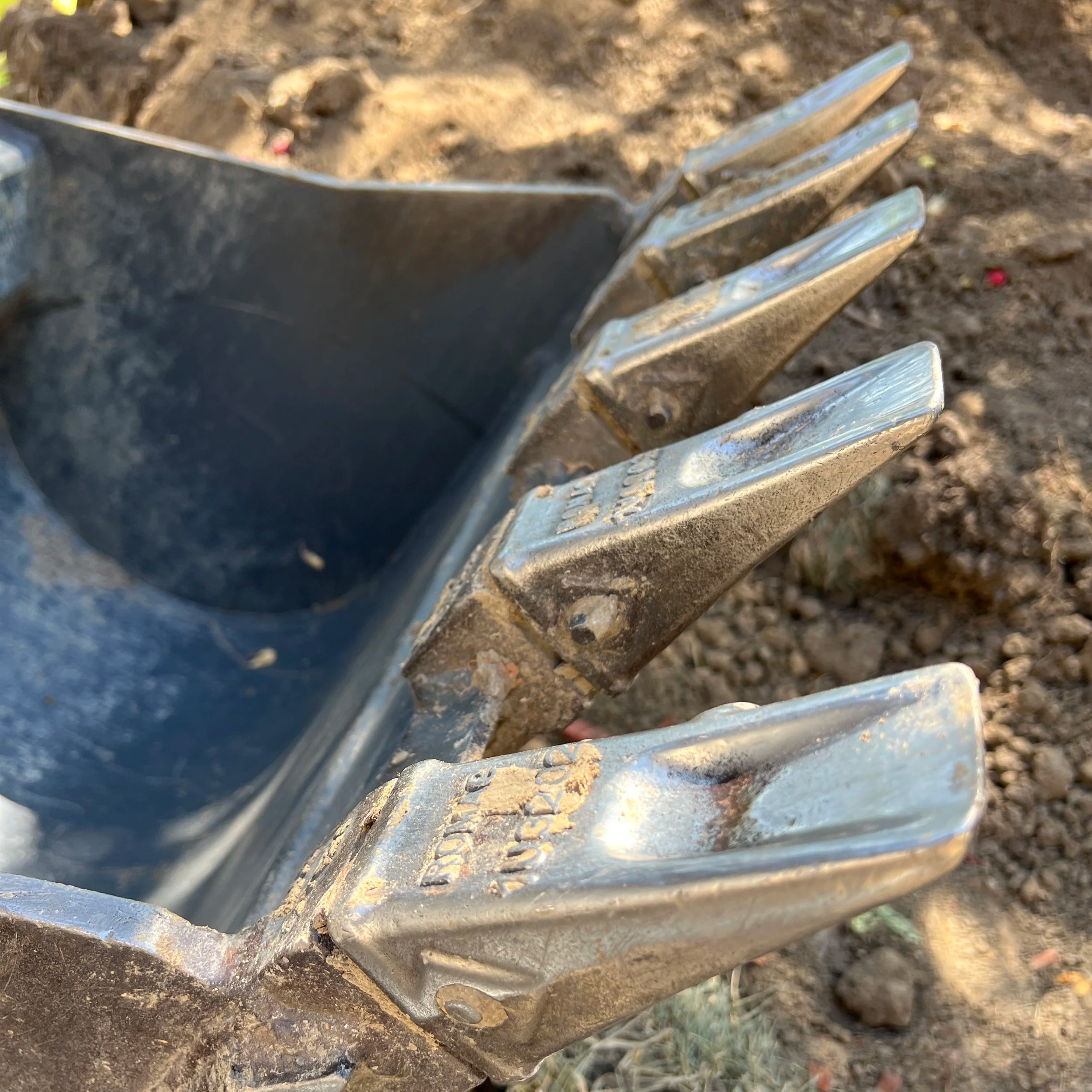 Close-up of a metal object with soil and dirt on it, possibly a tool or part of machinery, on the ground.