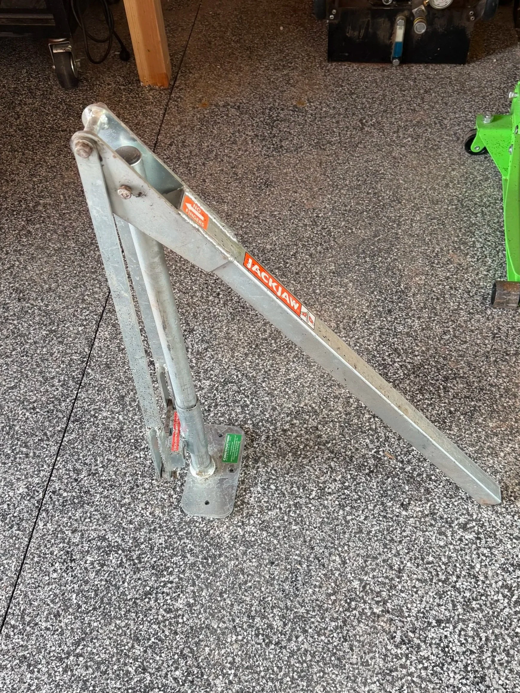 A silver aluminum ladder with safety stickers on a speckled black and white floor in a workshop or garage setting.