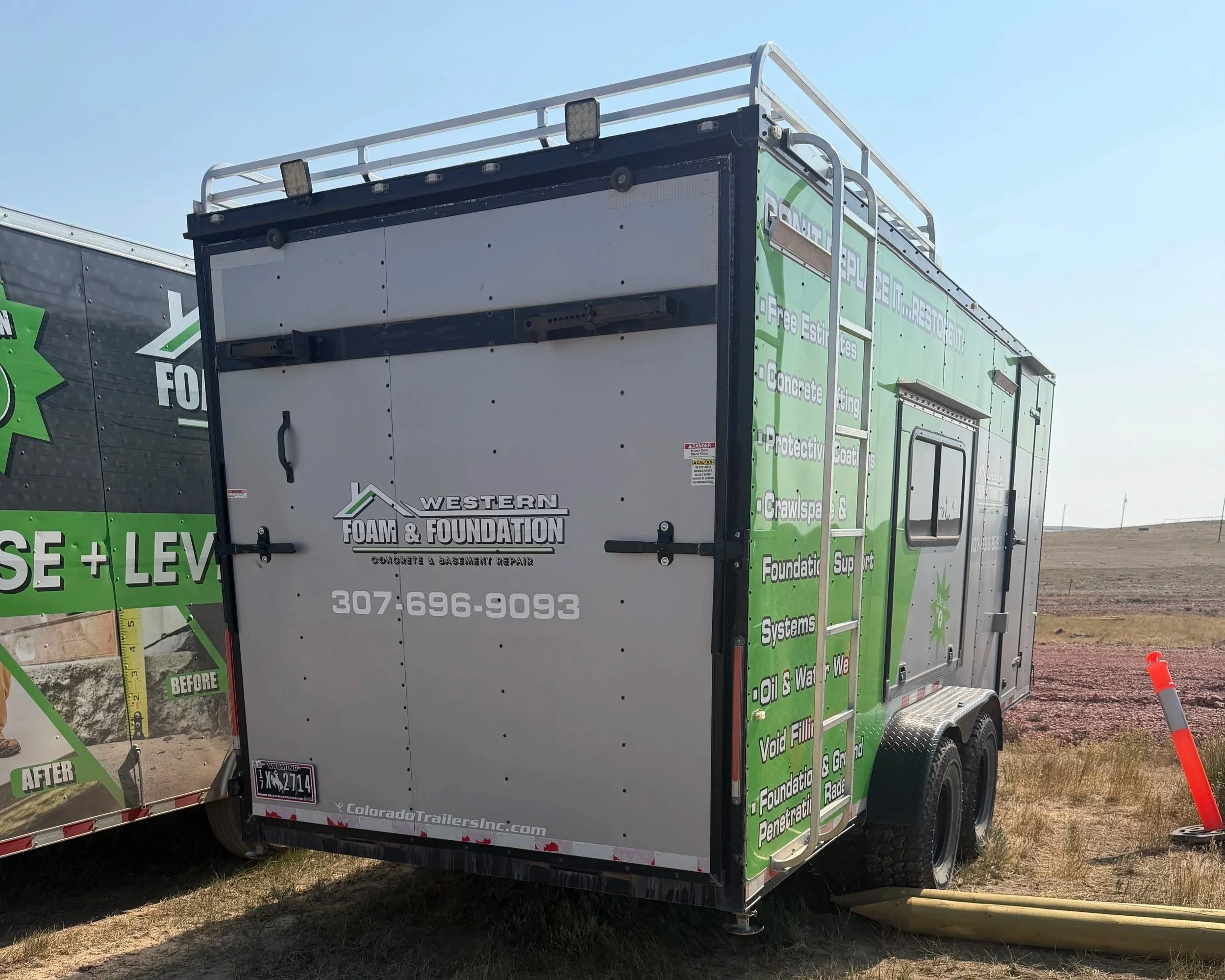 Mobile trailer with green and black branding for Western Foam & Foundation services, including concrete and basement repair, on a clear day at a construction or service site.