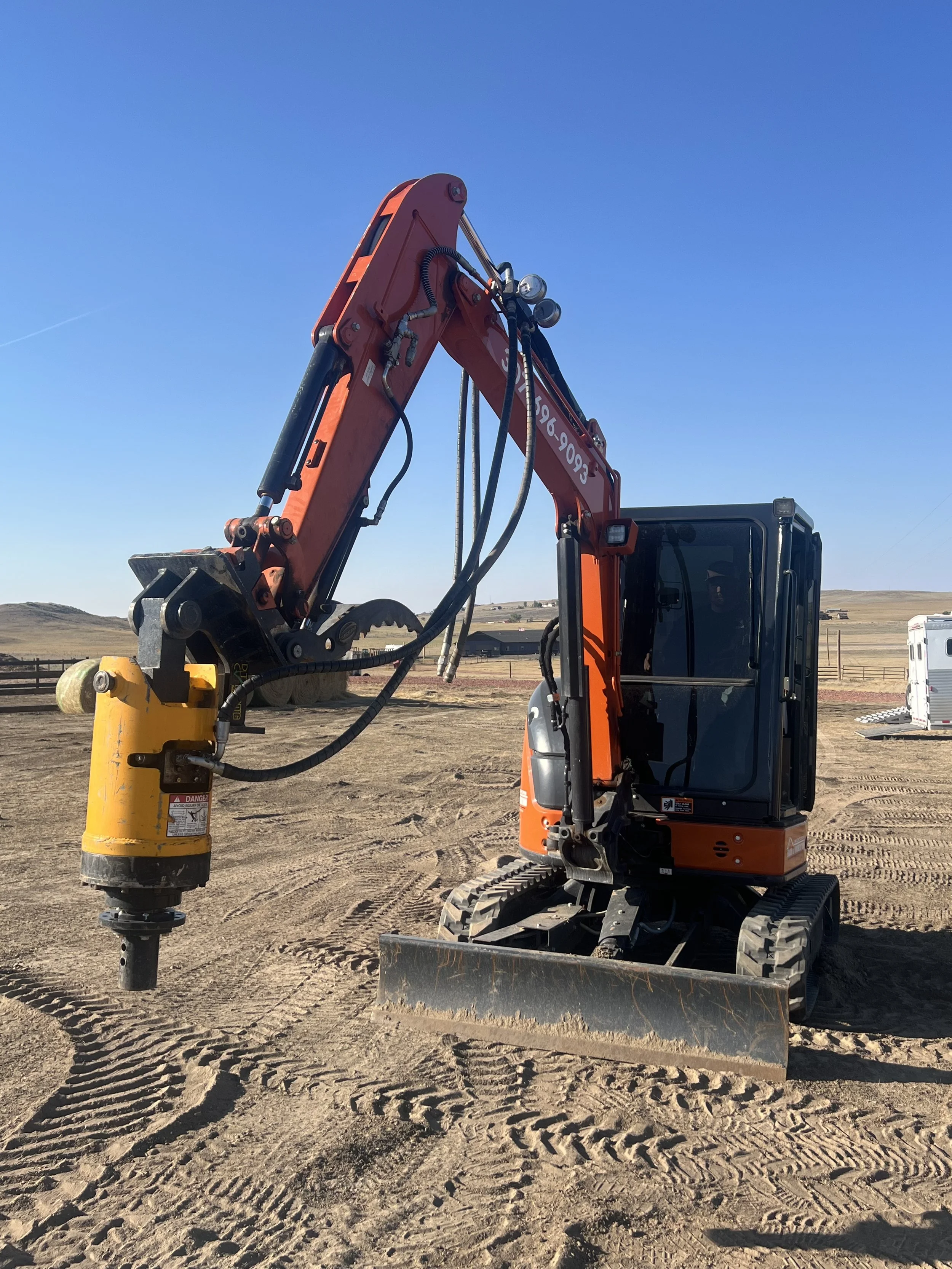 Hydraulic pump and hoses on dry, dusty ground, with a yellow component and pressure gauges visible.