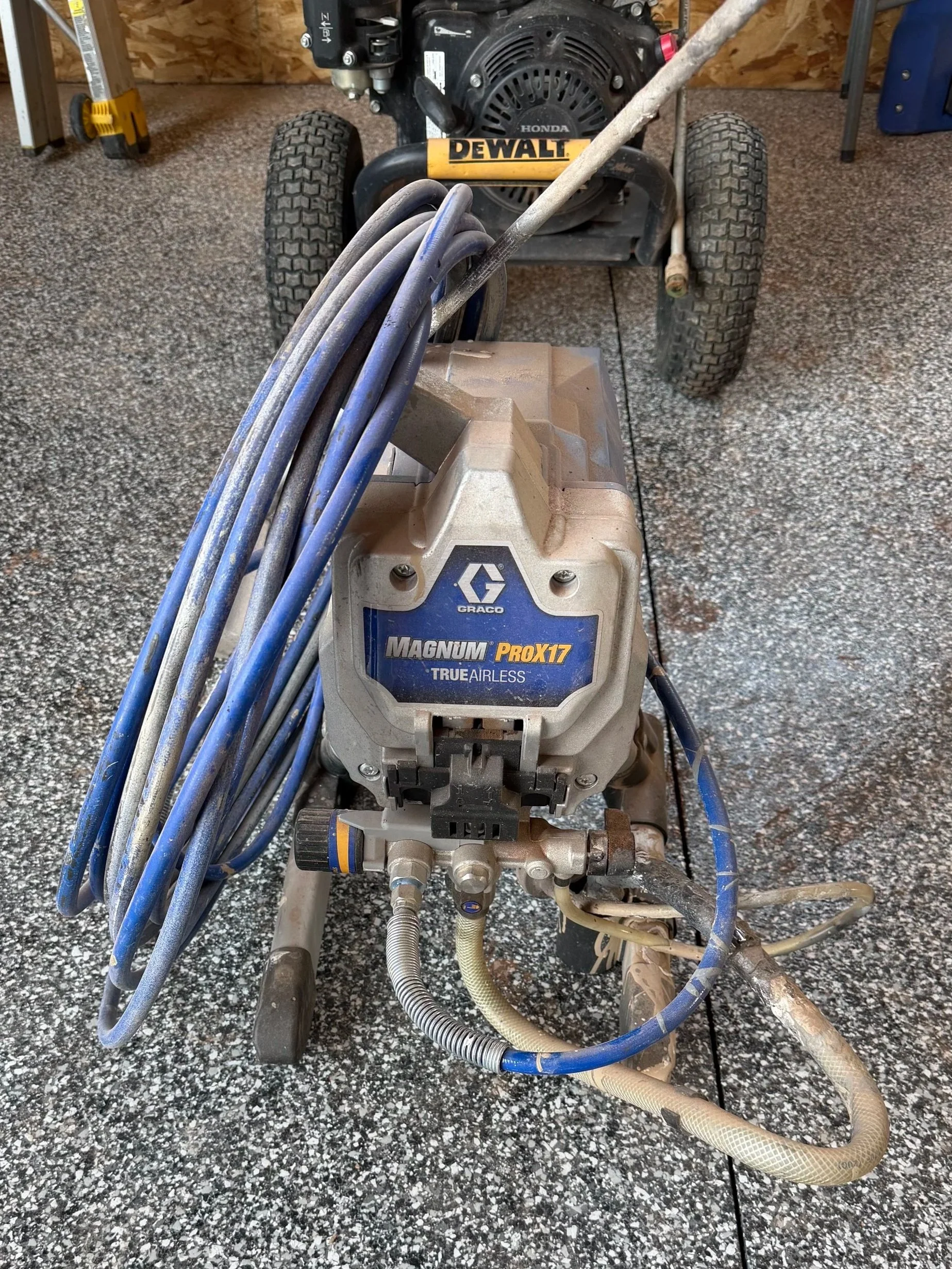 An industrial pressure washer with hoses and a spray wand, situated on a speckled black and white concrete floor. The machine is labeled 'Magnum ProX17' and features a Honda engine in the background.