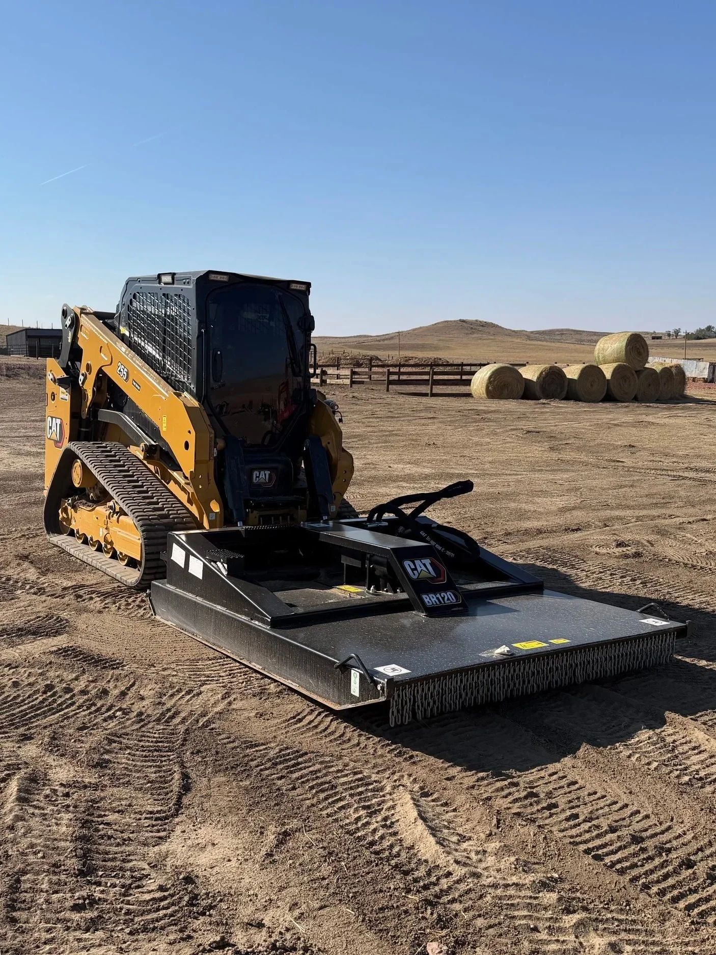 The image shows a piece of heavy machinery equipment, specifically a portion of a CAT construction attachment model BR120, set outdoors on dry, cracked ground. The equipment has hydraulic hoses, warning labels, and a metal frame with the CAT logo and model number visible.
