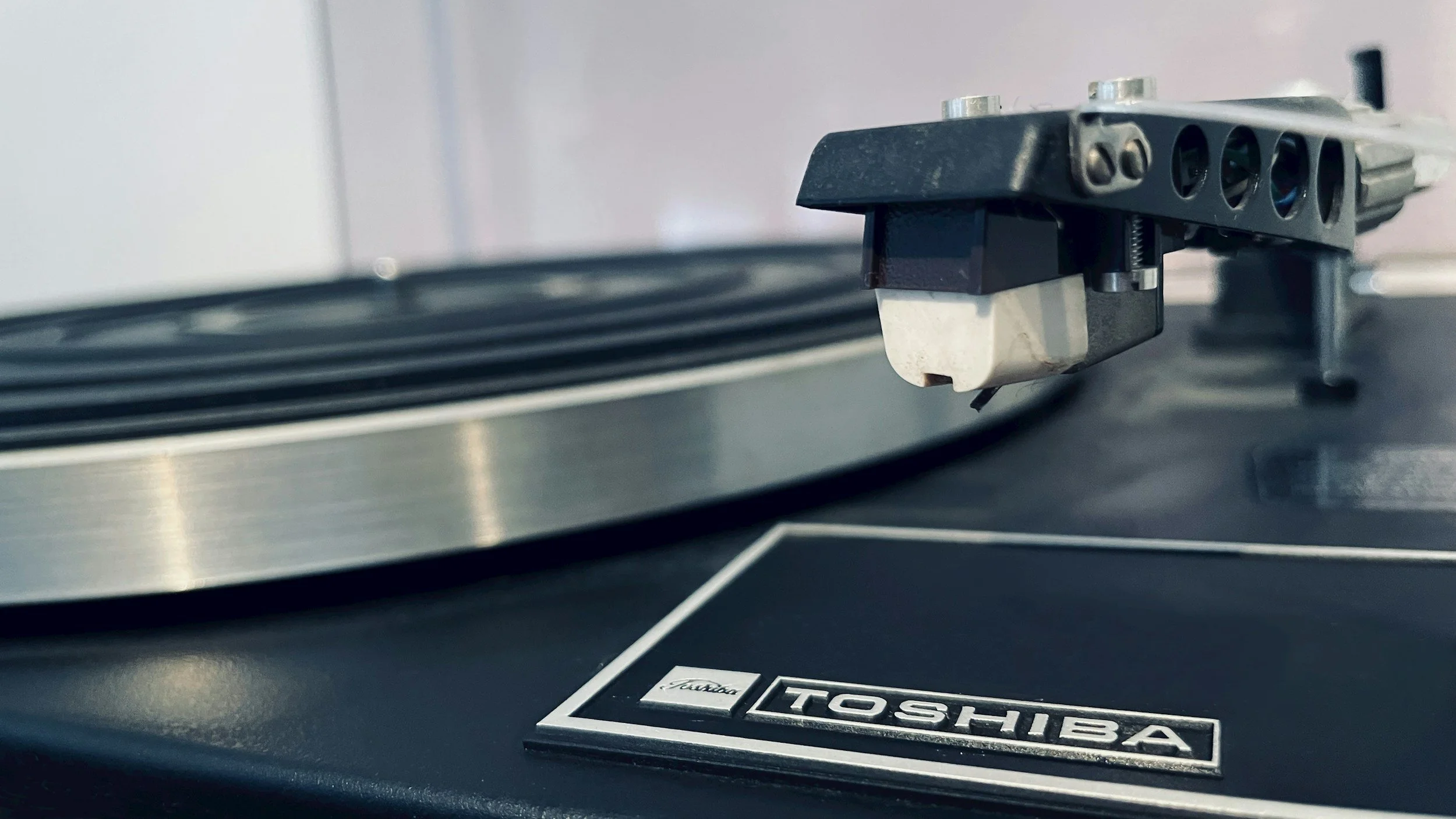 Close-up of a turntable tonearm with stylus over a vinyl record, featuring a Toshiba logo on the turntable base.