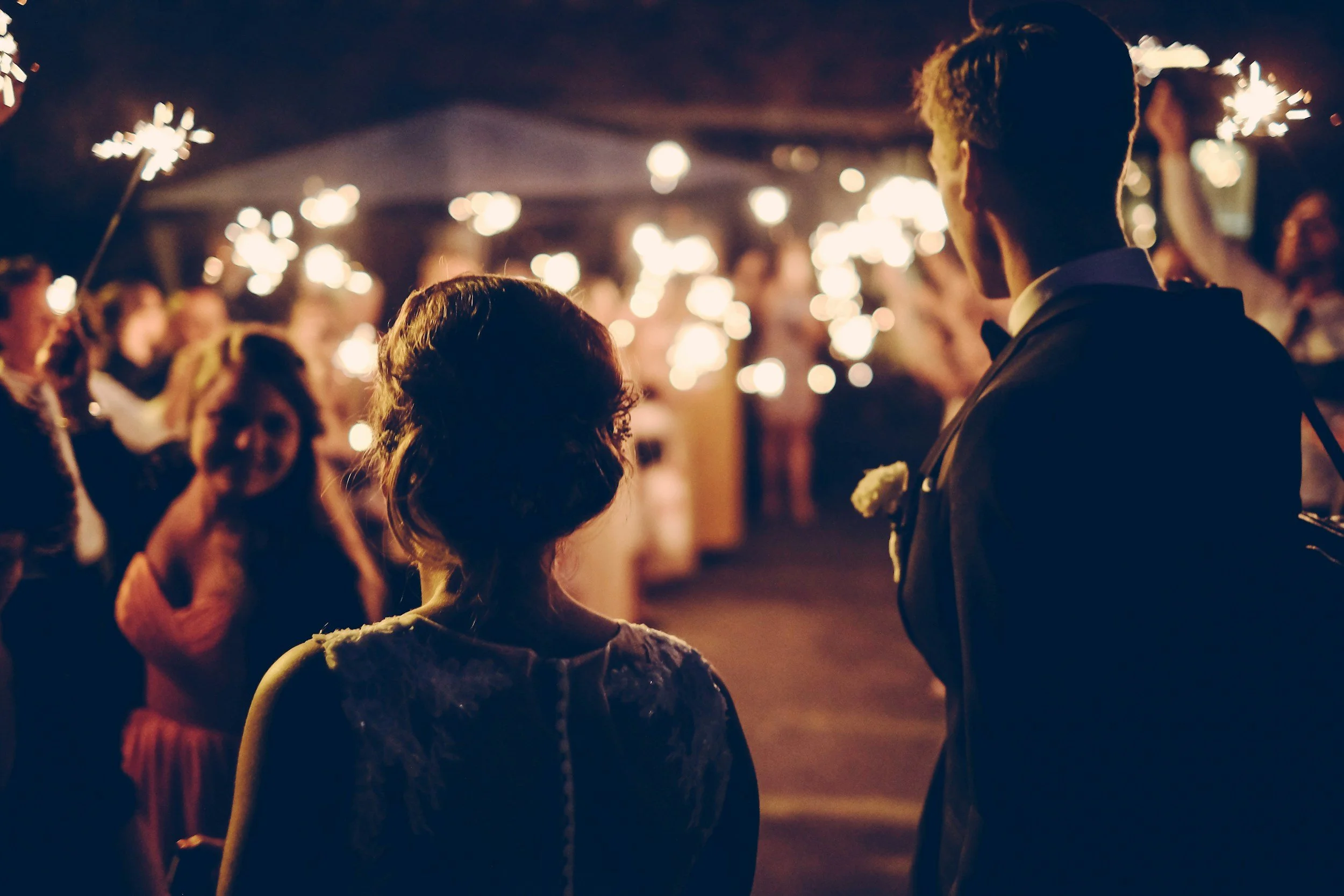 People celebrating at night with sparklers, wearing formal attire.