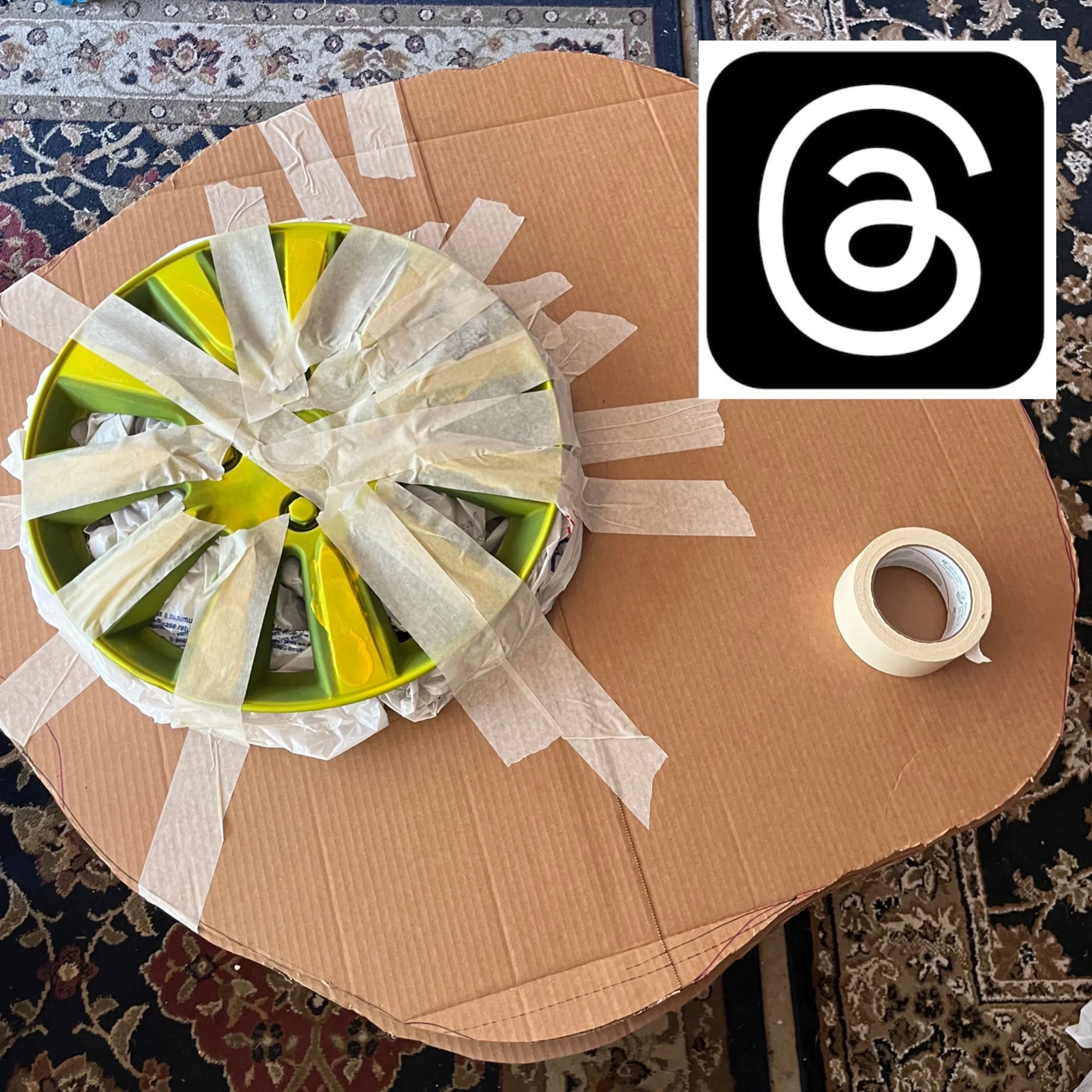 Yellow plastic hubcap taped to a cardboard surface, with a roll of masking tape nearby.