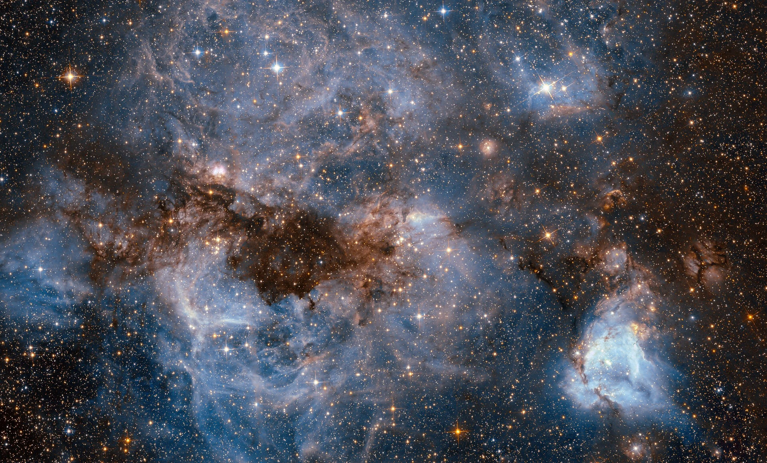 A detailed view of a star-forming region in space, showing numerous stars, nebulae, and cosmic dust clouds.