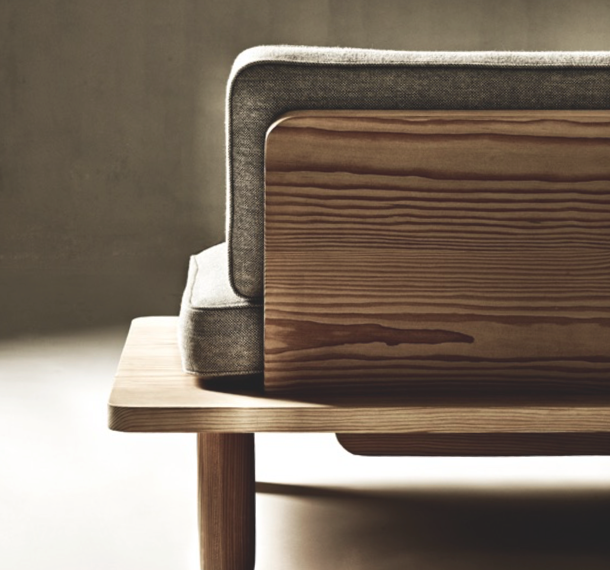Close-up of a table with layered wood patterns, a side view of a chair with fabric upholstery, and a backdrop of a neutral-colored background.