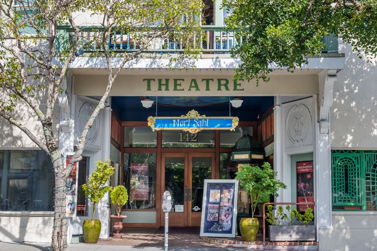 Entrance to a theatre with a sign for Mor Sah, potted plants, and posters outside.