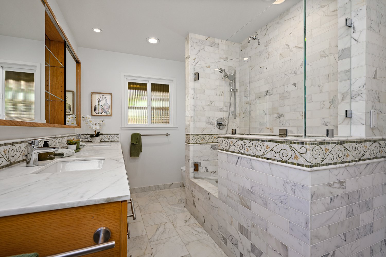 Modern bathroom with a marble vanity, large mirror, and a glass-enclosed shower with marble tile walls and decorative border.
