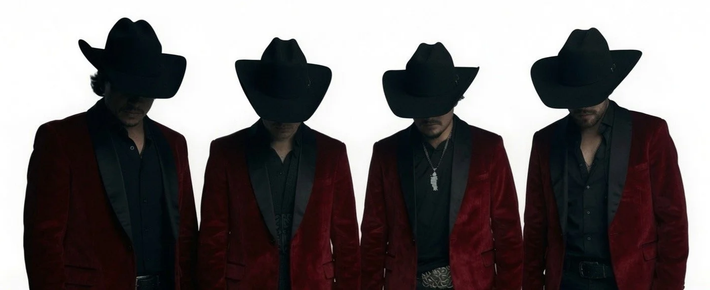 Four men dressed in black shirts and red velvet jackets with black satin lapels, wearing large black cowboy hats, standing side by side against a plain white background.