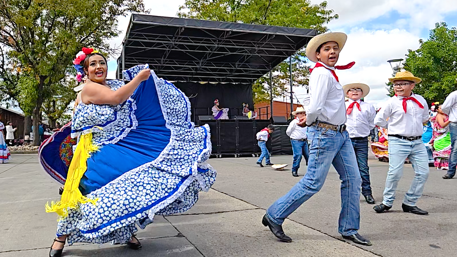 People dressed in traditional Mexican clothing performing a folkloric dance outdoors during a celebration or festival.