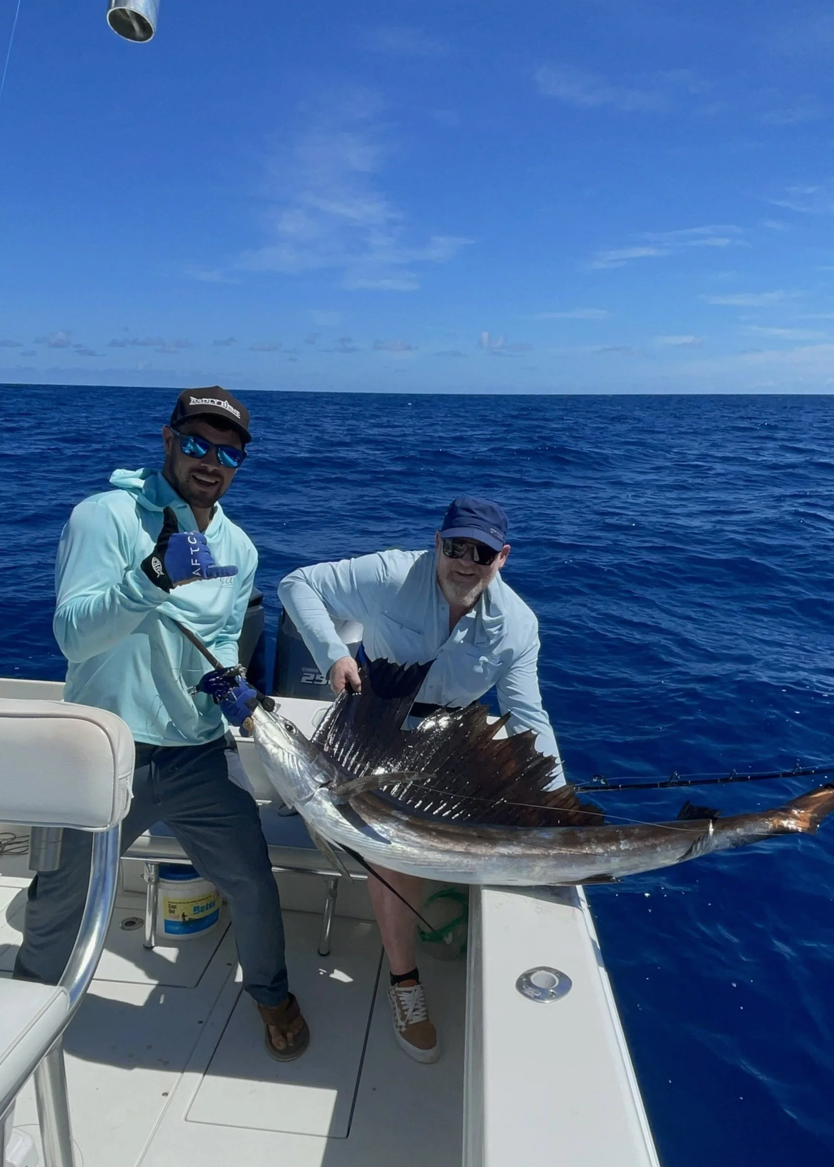 Two men on a boat holding a large fish, with water and sky in the background.