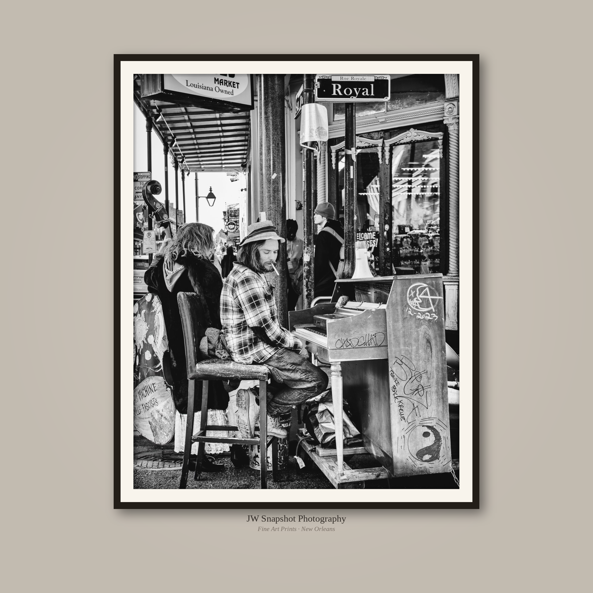 Black and white photo of storefront with people sitting outside, including a man playing piano and a woman with a hat, with street signs reading 'Royal' and 'Louisiana Owned'.