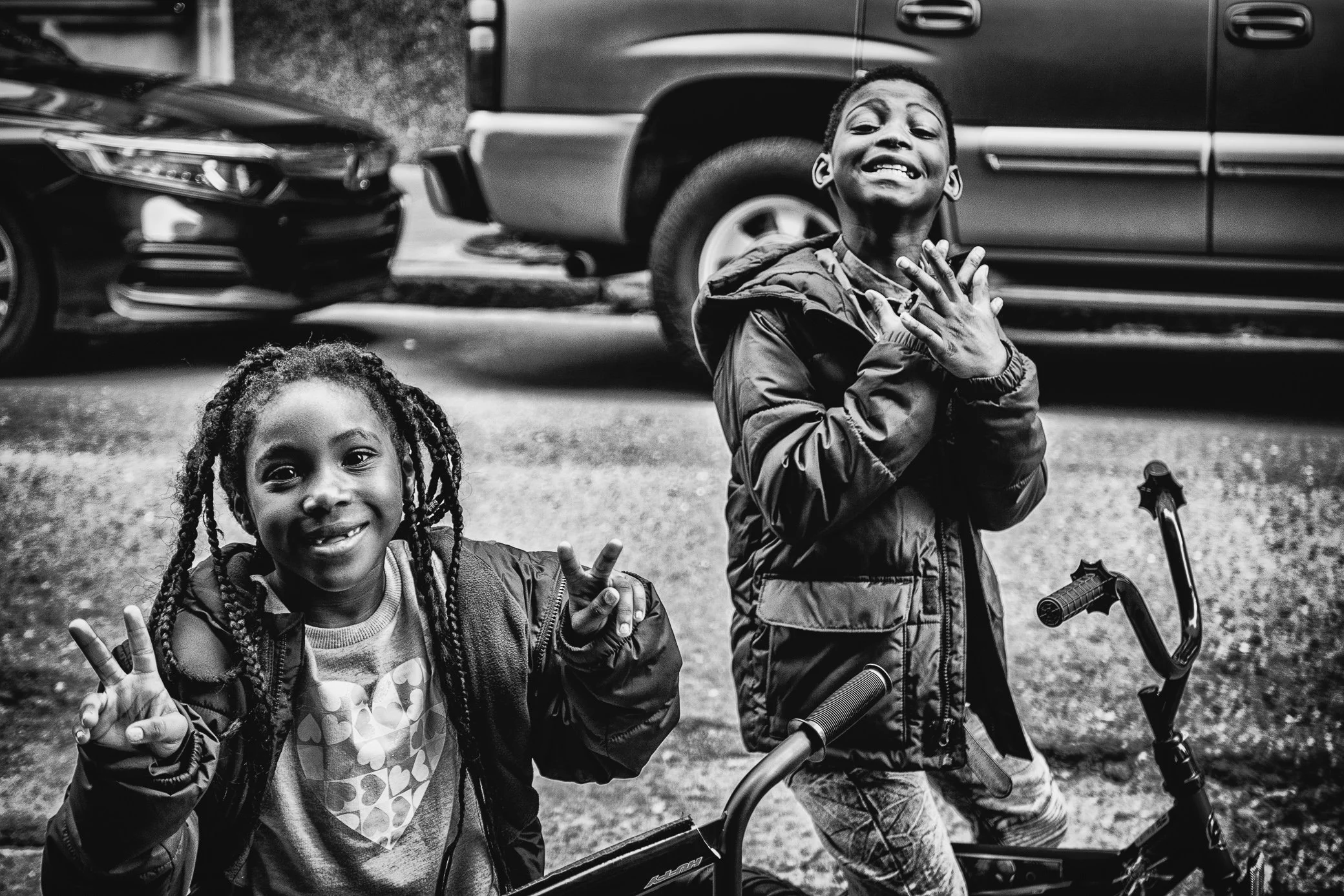 Two children with their bicycles grin at the camera, the girl flashing peace signs, New Orleans.