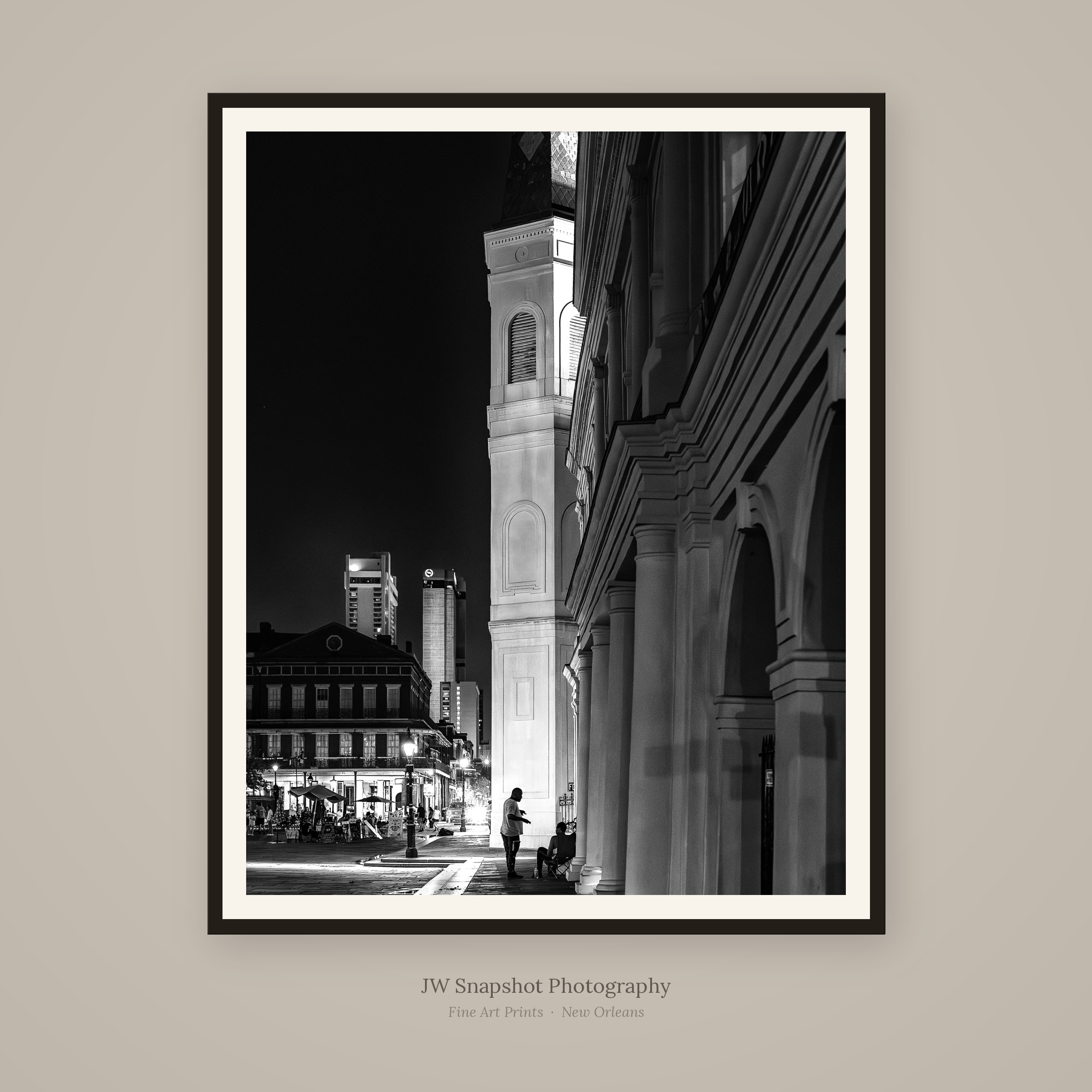 Black and white night photograph of a city street with historic architecture, people walking and sitting outdoors, and modern skyscrapers in the background.