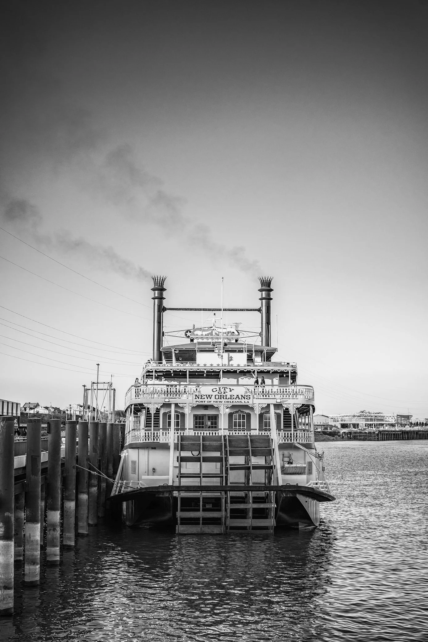 A black and white photo of a riverboat docked at a pier, with signs indicating it is in New Orleans, Louisiana.